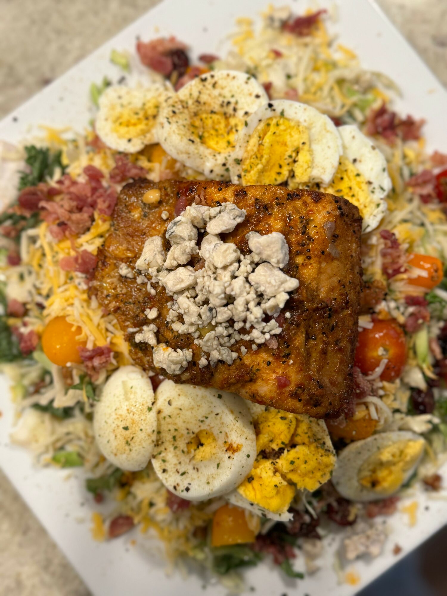 Grilled fish fillet topped with crumbled cheese, served on a bed of salad with sliced boiled eggs and cherry tomatoes.