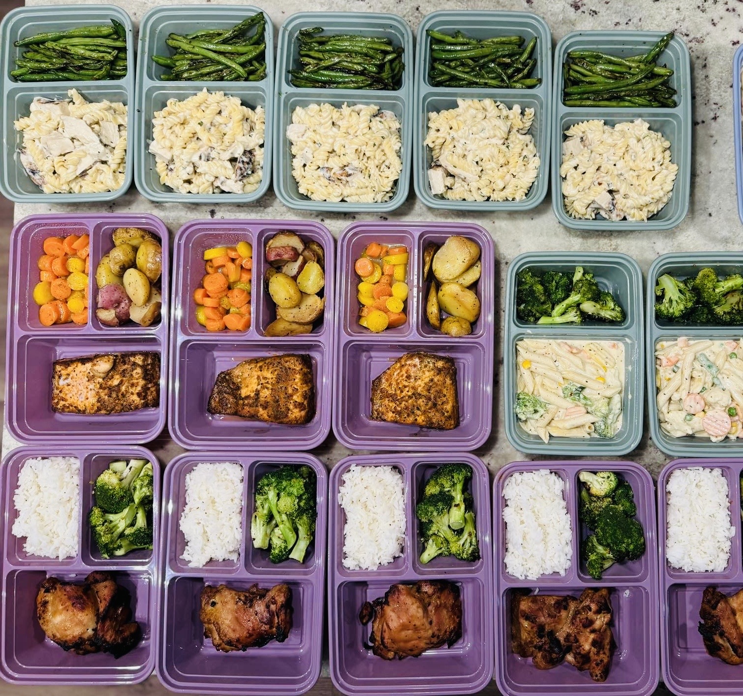 Meal prep containers with vegetables, rice, and chicken arranged in rows, viewed from above.