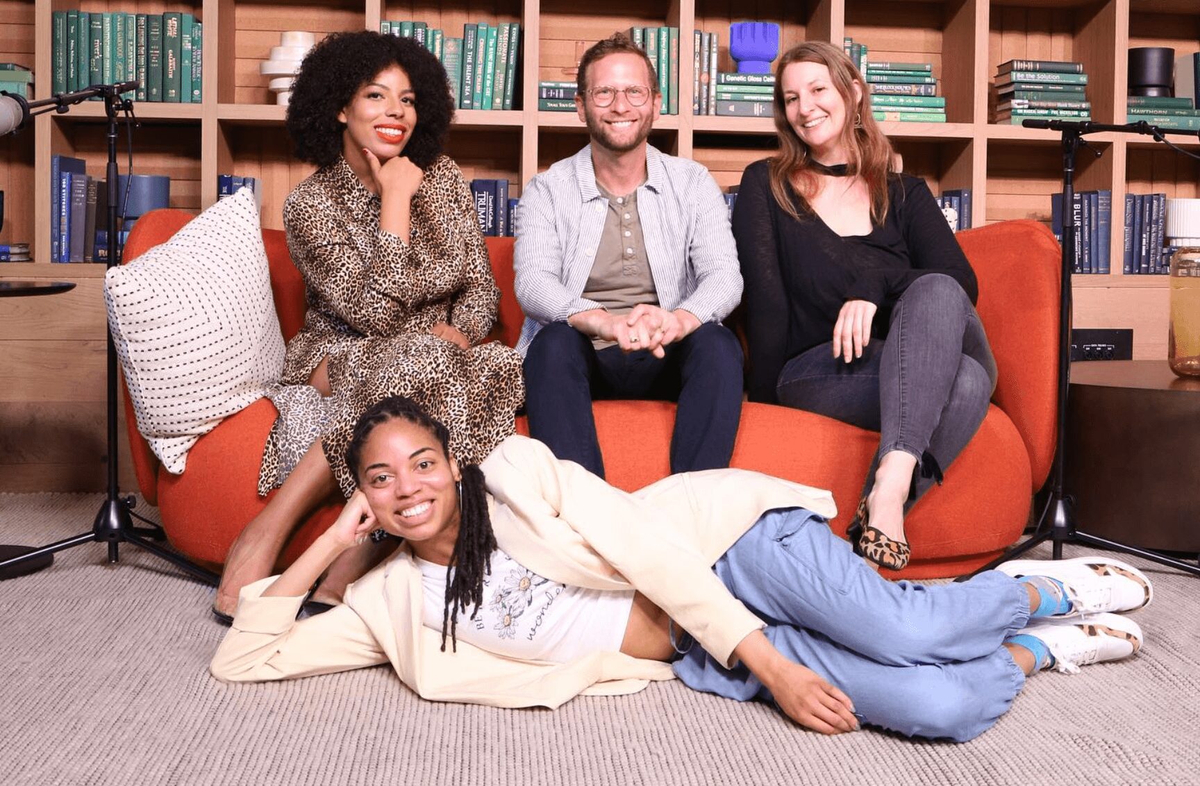Four people sitting and lying on a sofa in a room with bookshelves, smiling and posing for the photo.