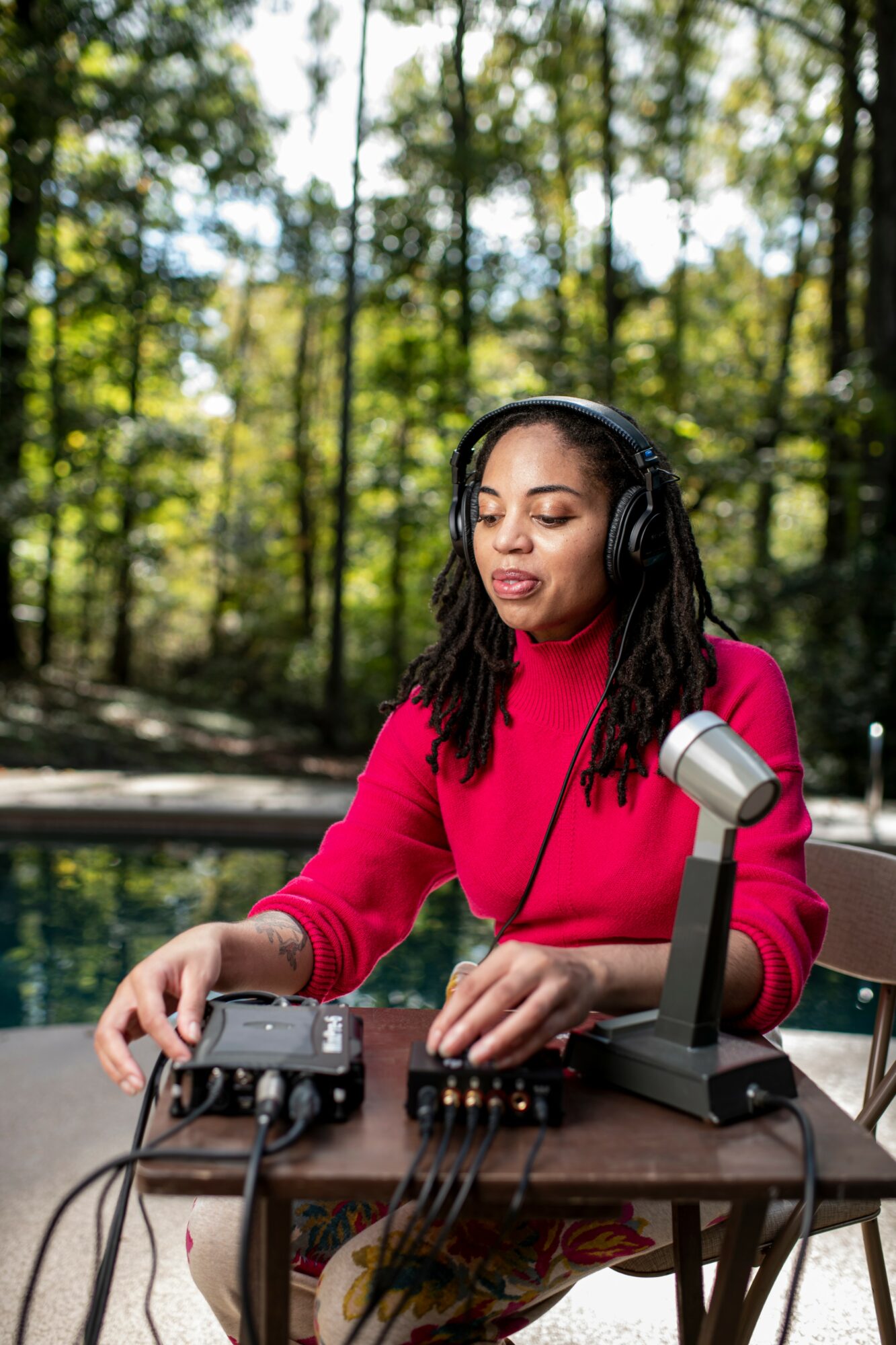 Woman with headphones operating audio equipment outdoors in a forest setting.