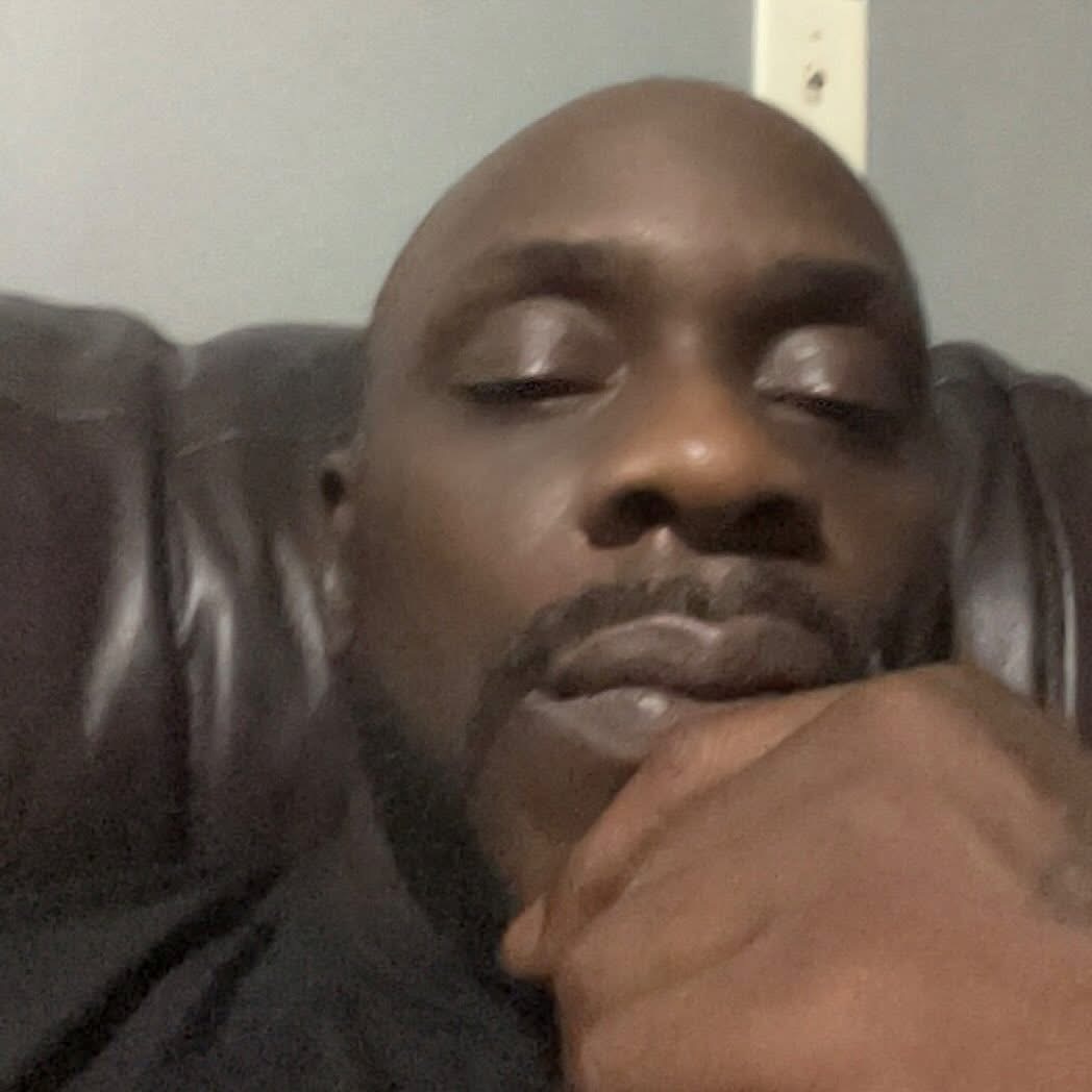 Close-up of a man resting his chin on his hand, eyes partially closed, sitting on a dark leather chair.