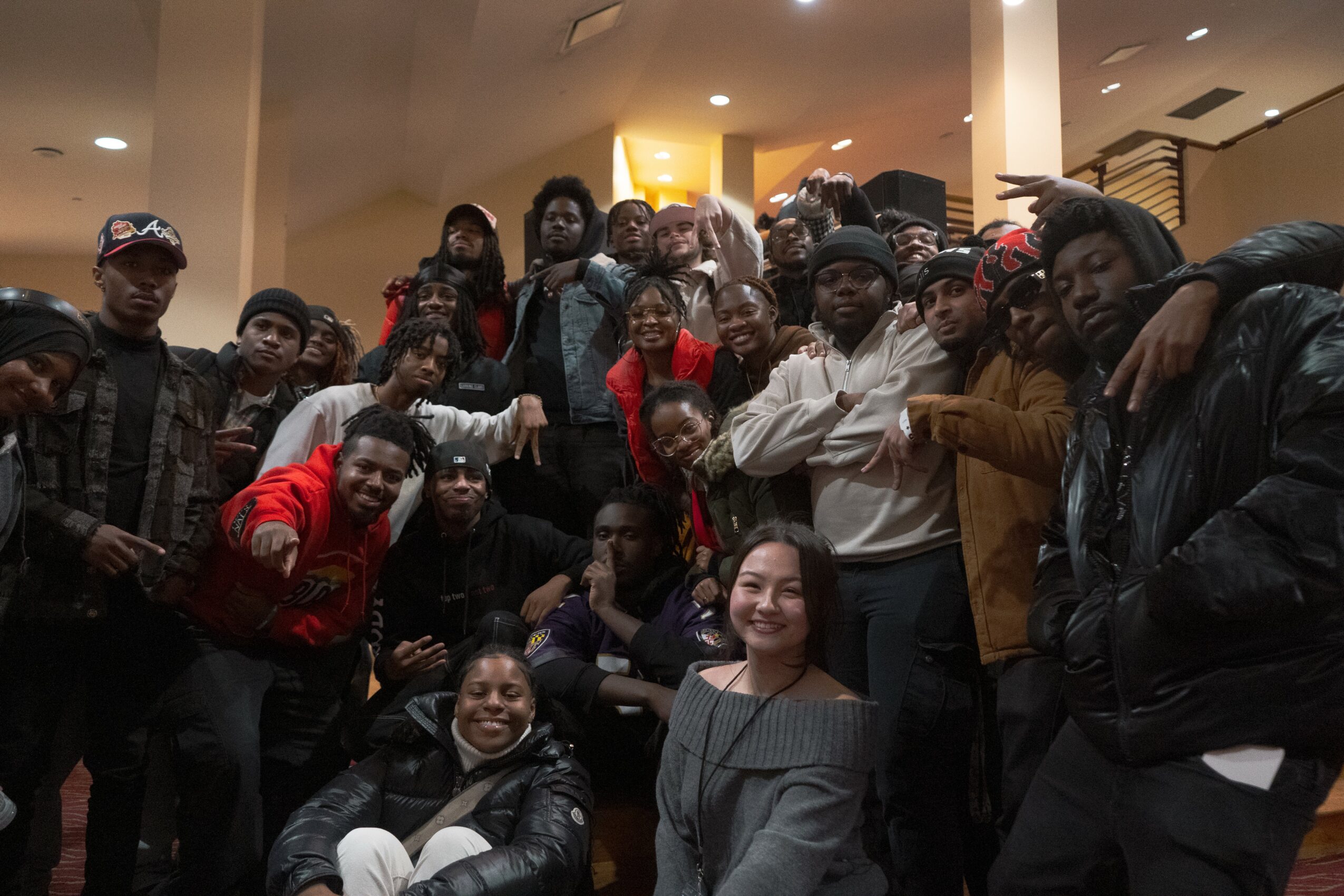 Group of people gathered indoors, some smiling and posing for the photo, with a warm lighting background.