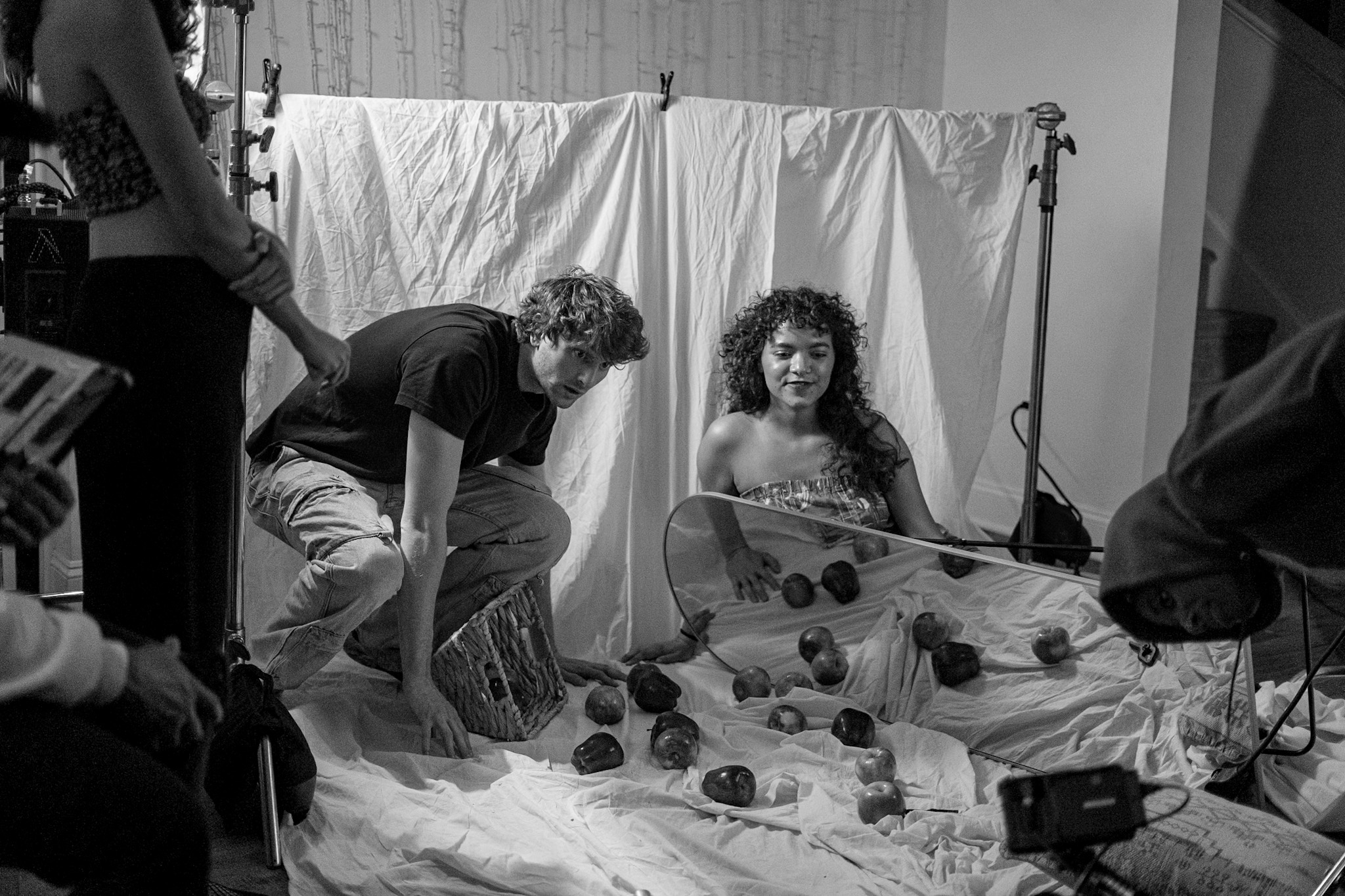 Person and woman with curly hair in a photography studio with roses on the floor, white backdrop, and equipment.