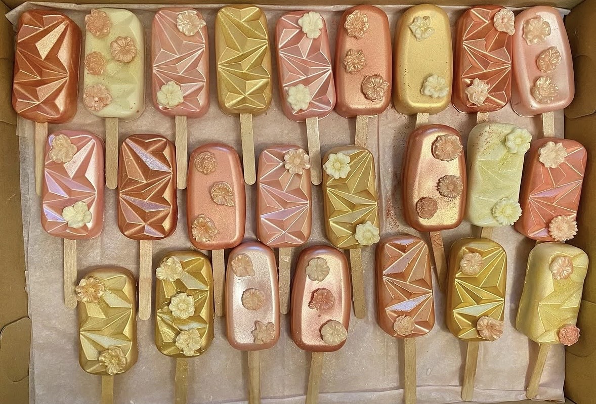 Assorted colorful ice cream bars with various toppings on sticks, arranged in rows.