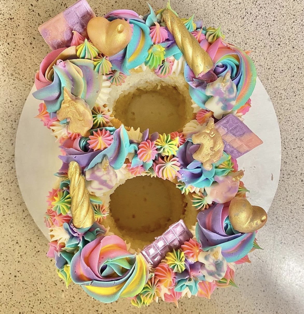 Colorful number 8 cake decorated with pastel frosting, candies, and gold accents, on a white surface.