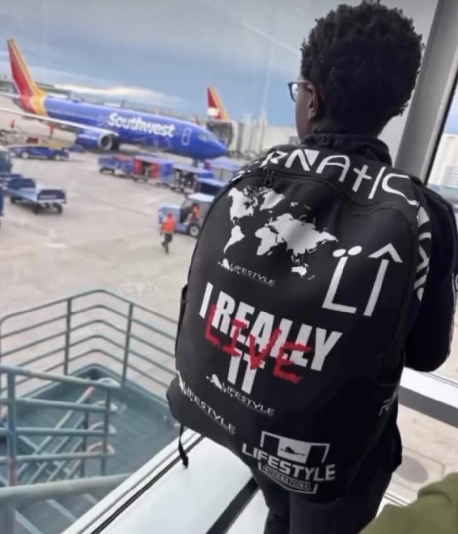 Person with curly hair and glasses looking at airplanes through a window at the airport.