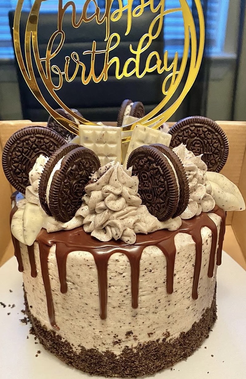 Chocolate and vanilla birthday cake with Oreo cookies, whipped cream, and a gold 'happy birthday' topper.