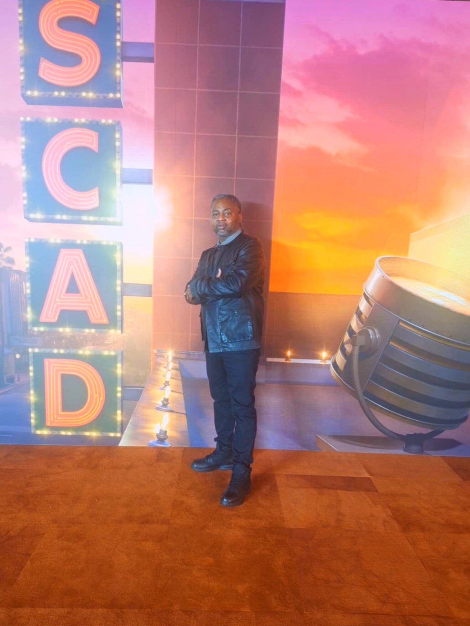 Person standing on stage with colorful background and large illuminated letters spelling 'S C A D'.
