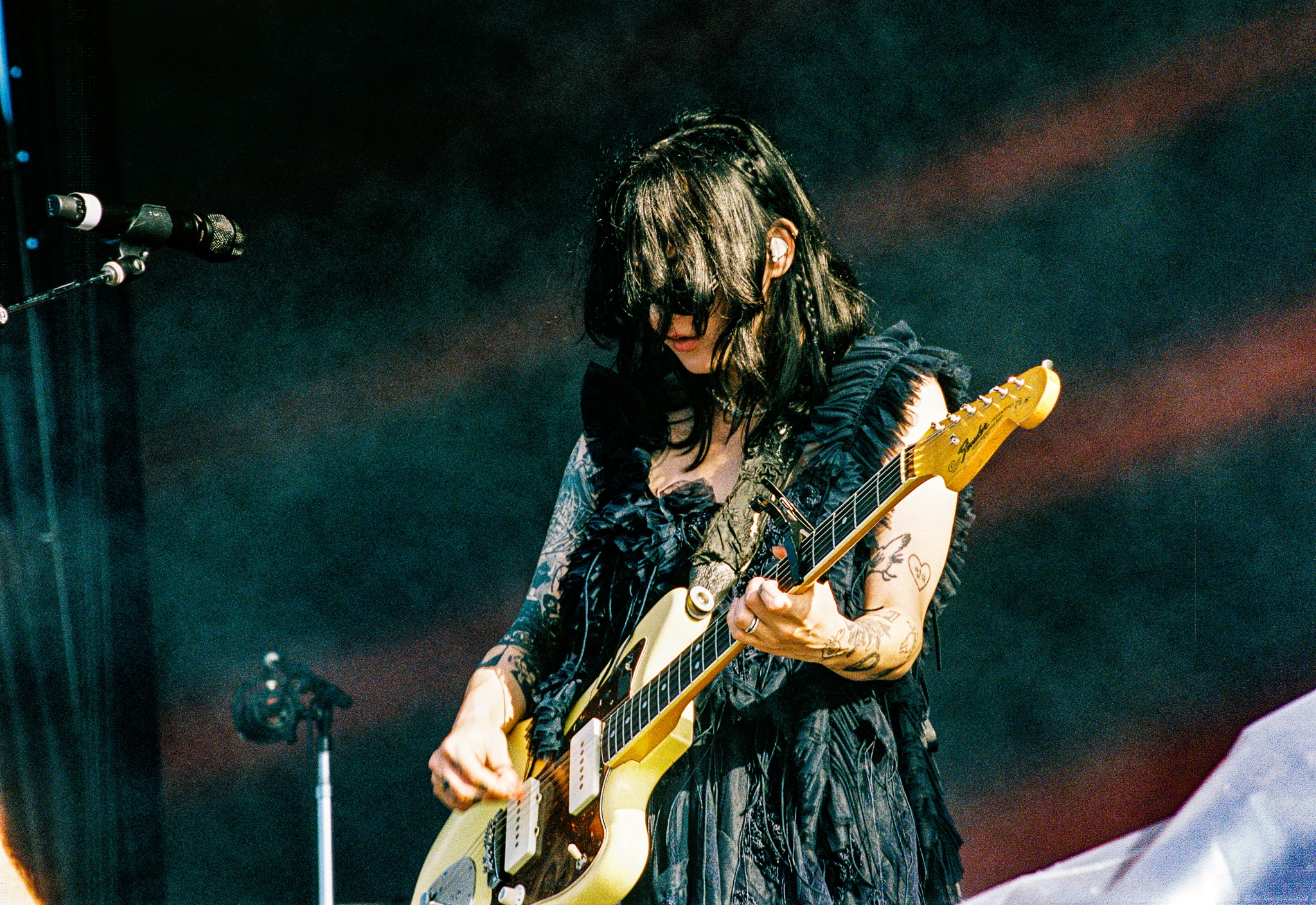 Person playing electric guitar on stage with dark background and stage lighting.