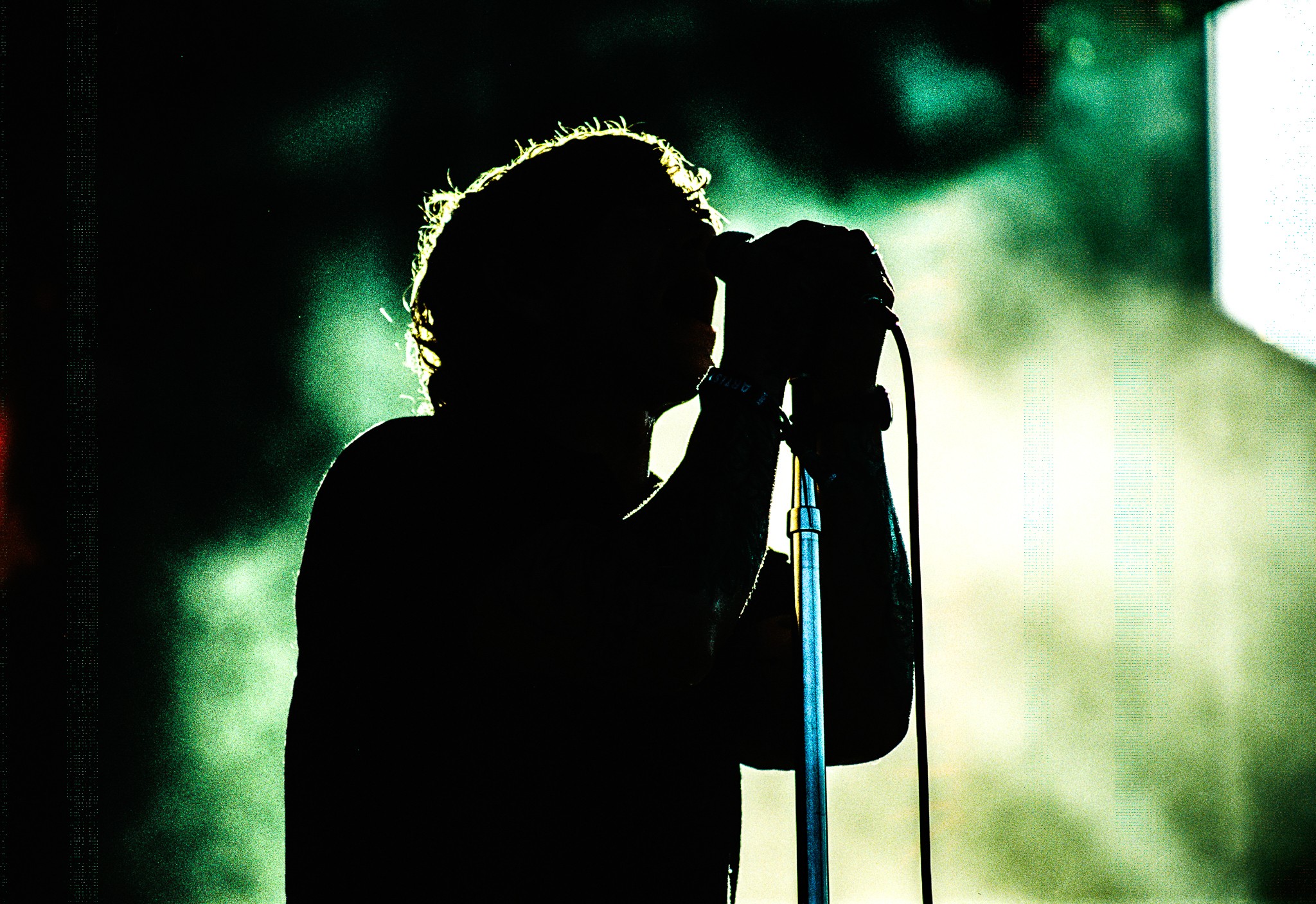 Silhouette of a person singing into a microphone with a bright background, possibly outdoors or on stage.