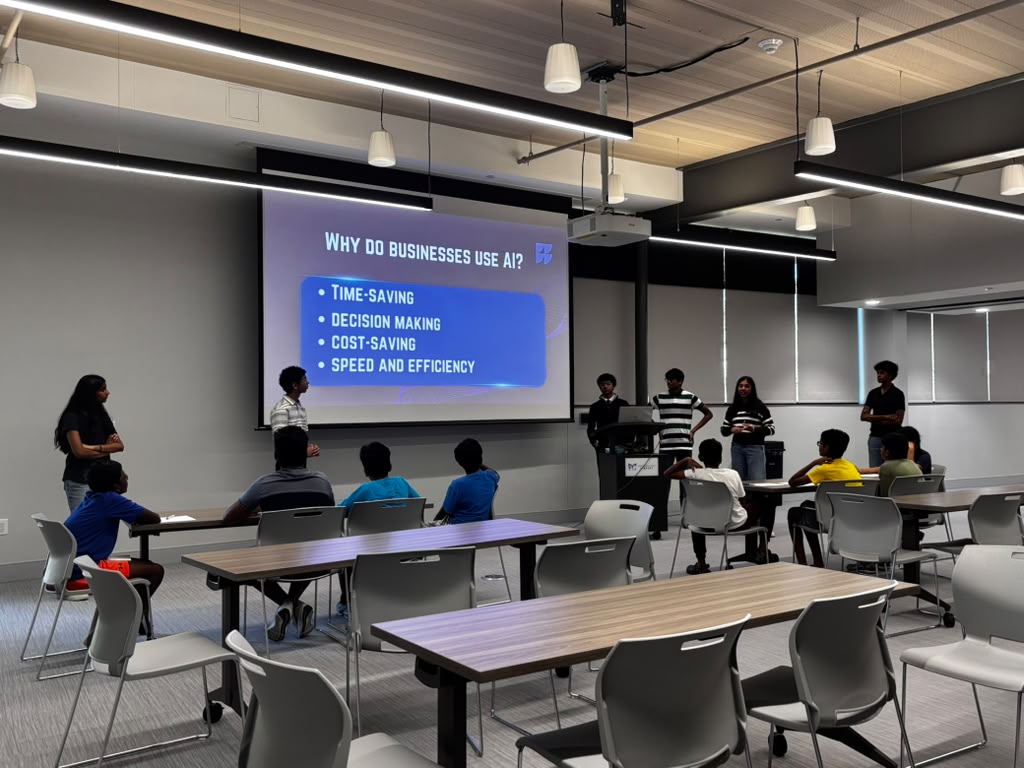Classroom with students and presenters, large screen displays reasons for using business apps, including time-saving and decision-making.