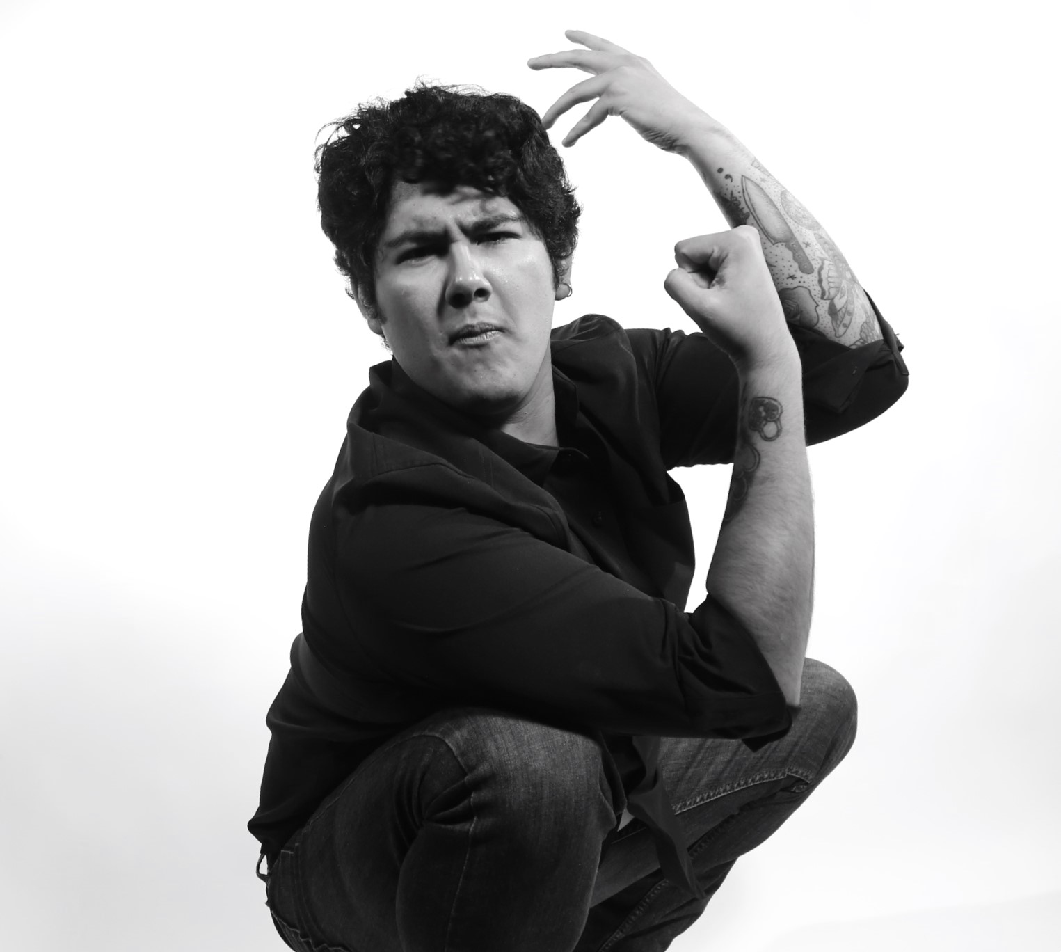 Person crouching with one arm raised and fist clenched, looking at the camera, black and white image.