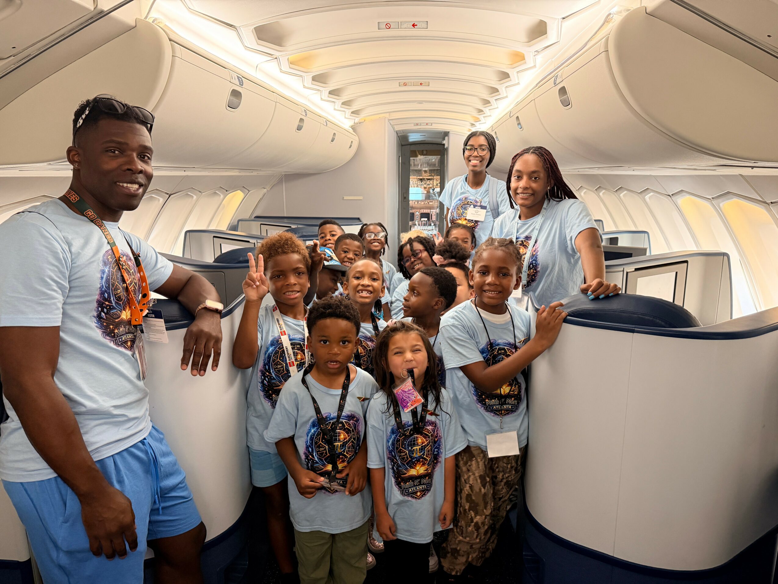 Group of children and adults inside an airplane cabin, smiling and posing for a photo.