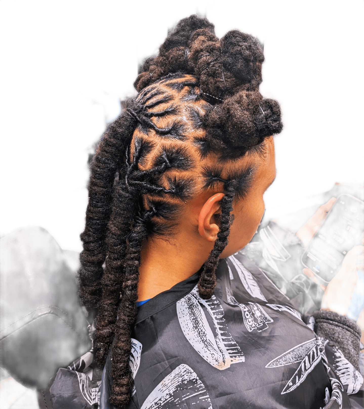 Person with styled dreadlocks and a top bun, wearing a patterned shirt, viewed from the back.