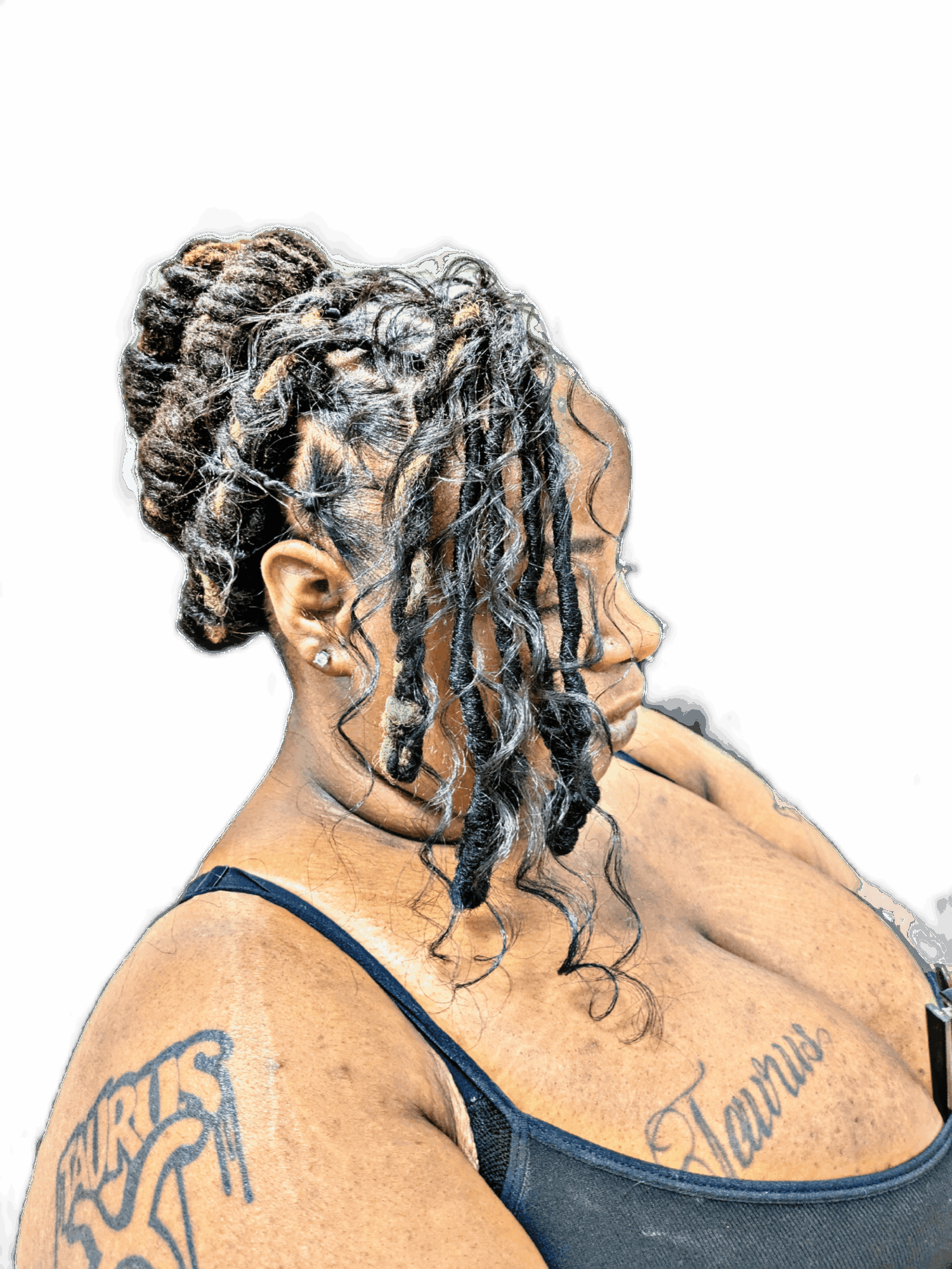 Side profile of a woman with dreadlocks styled in an updo, tattoos on her shoulder and chest, wearing a dark top, against a black background.
