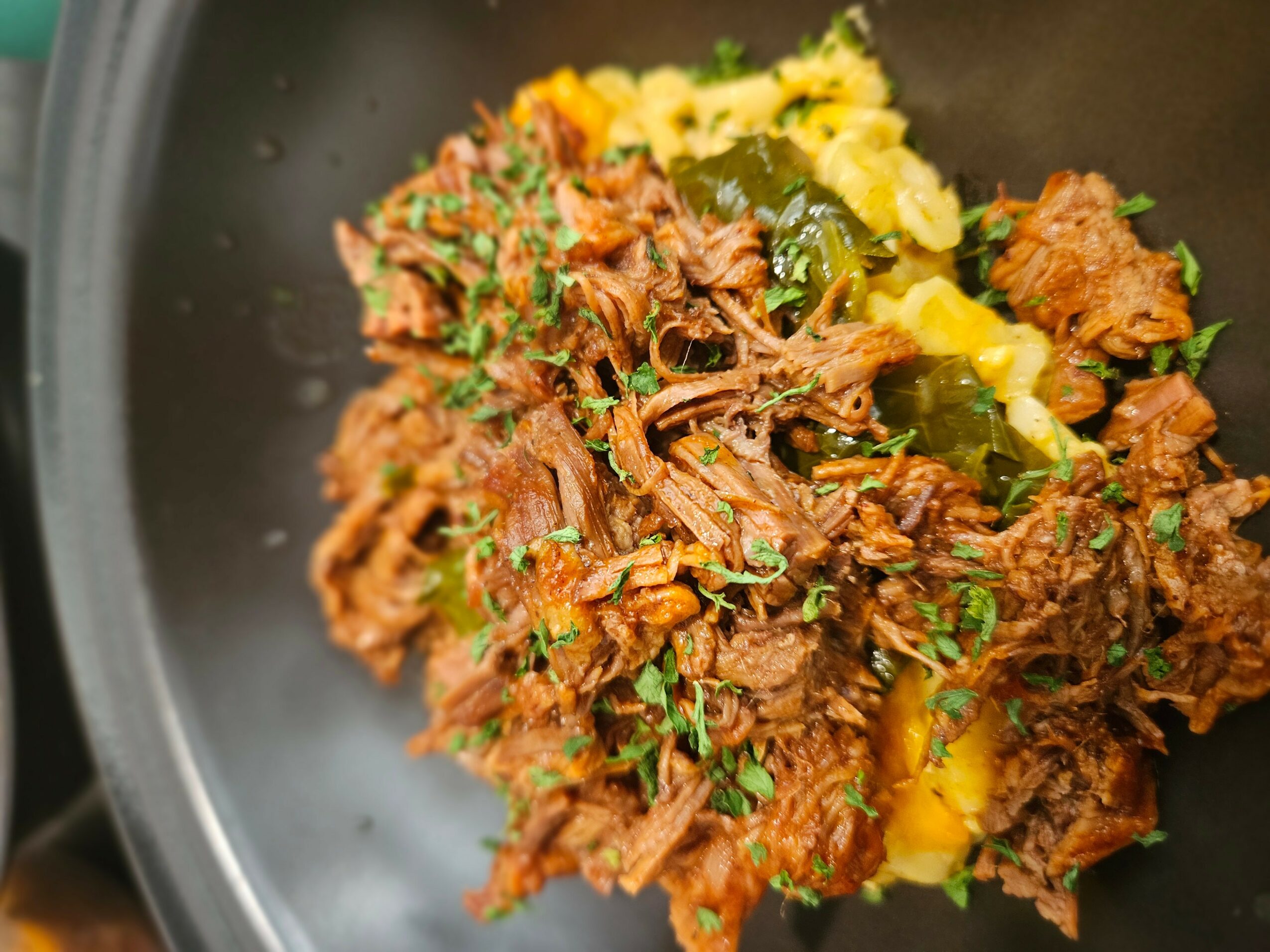 Cooked shredded meat with herbs and vegetables in a black pan.
