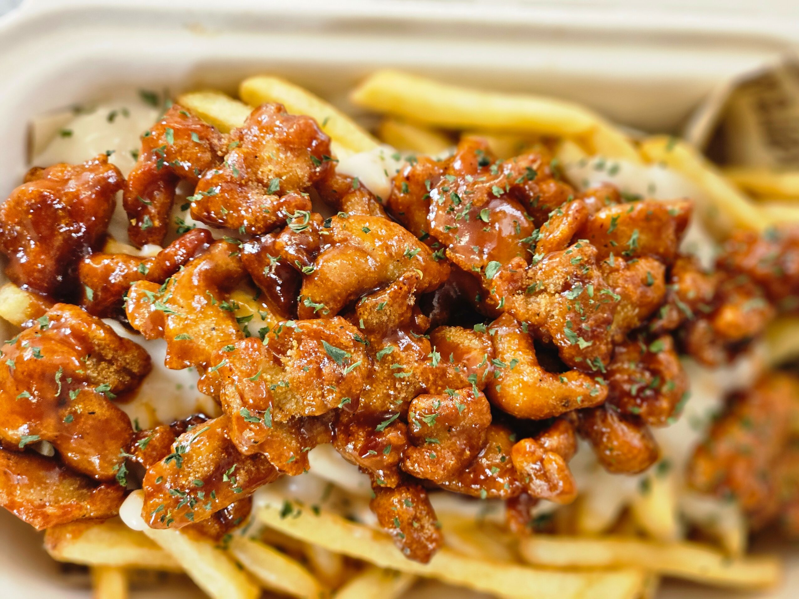 Close-up of seasoned, cooked meat pieces on a bed of fries or chips, with some herbs visible.