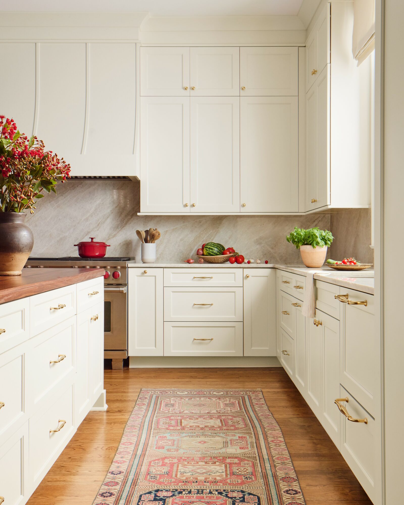 Bright kitchen with white cabinets, wooden floor, and a pink patterned rug, featuring a window with natural light.