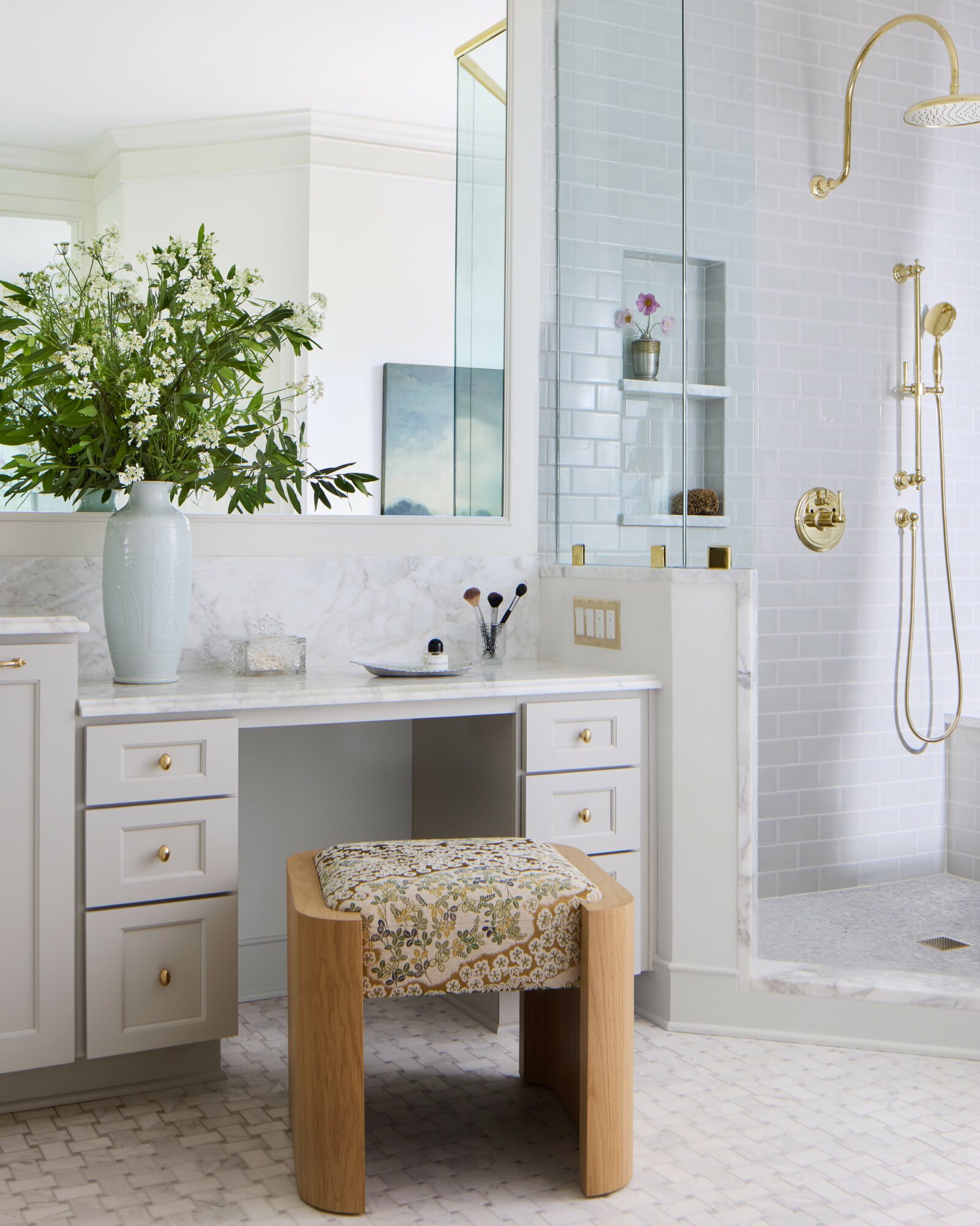 Bathroom vanity with a large vase of flowers, mirror, and a stool in front, with a shower area visible on the right.