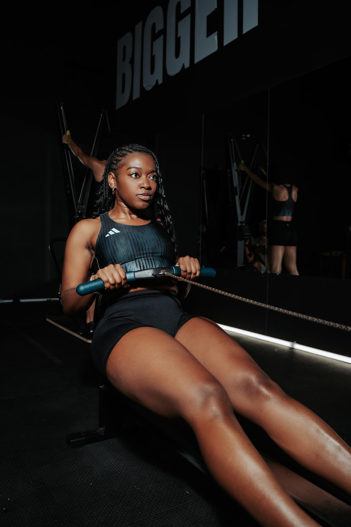 Young woman using a rowing machine in a gym, with a mirror reflecting her and the gym environment.