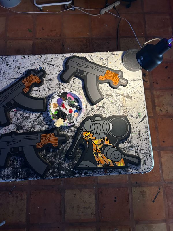 Table with paper gun cutouts, a round container, and a black object, on a tiled floor.