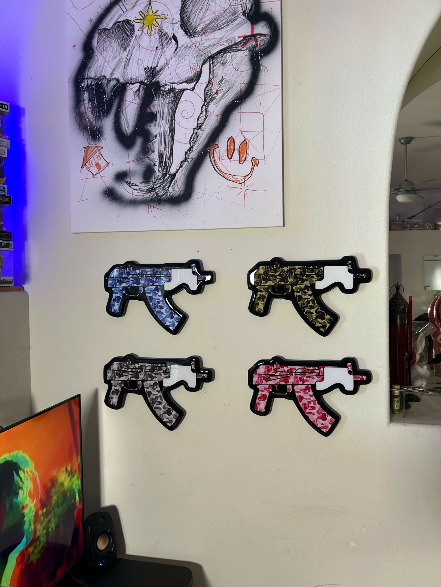 Four decorative gun-shaped objects on a wall, arranged in two rows, with a colorful abstract painting above and a TV below.