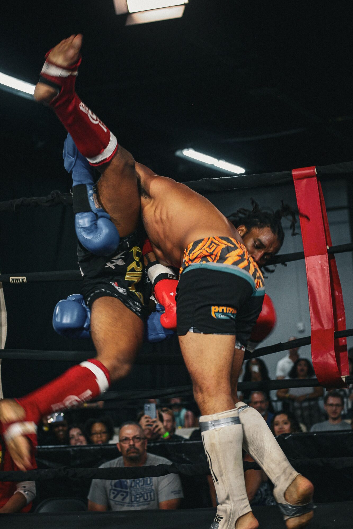 Two male fighters in a boxing ring engaged in a match, one delivering a punch to the other's face, audience watching.
