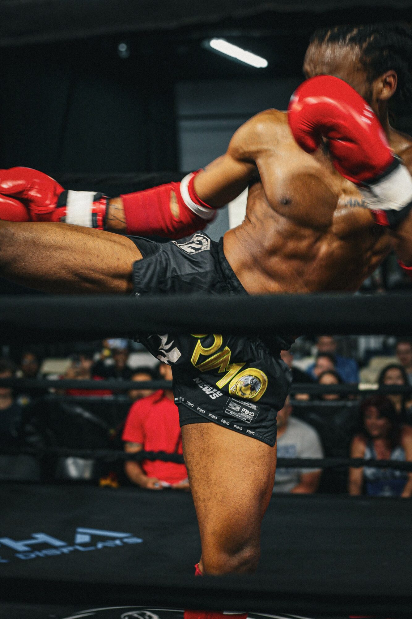 Female Muay Thai fighter delivering a high kick to opponent's head in a boxing ring, wearing red gloves and shorts.
