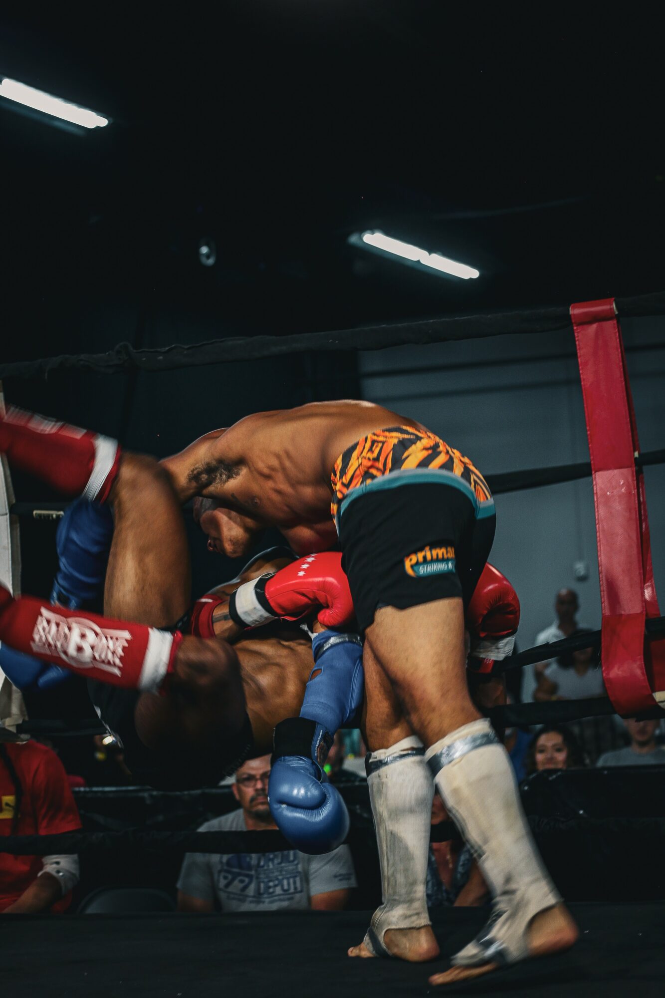 Two boxers engaged in a match inside a boxing ring, with one delivering a punch to the other, surrounded by spectators.