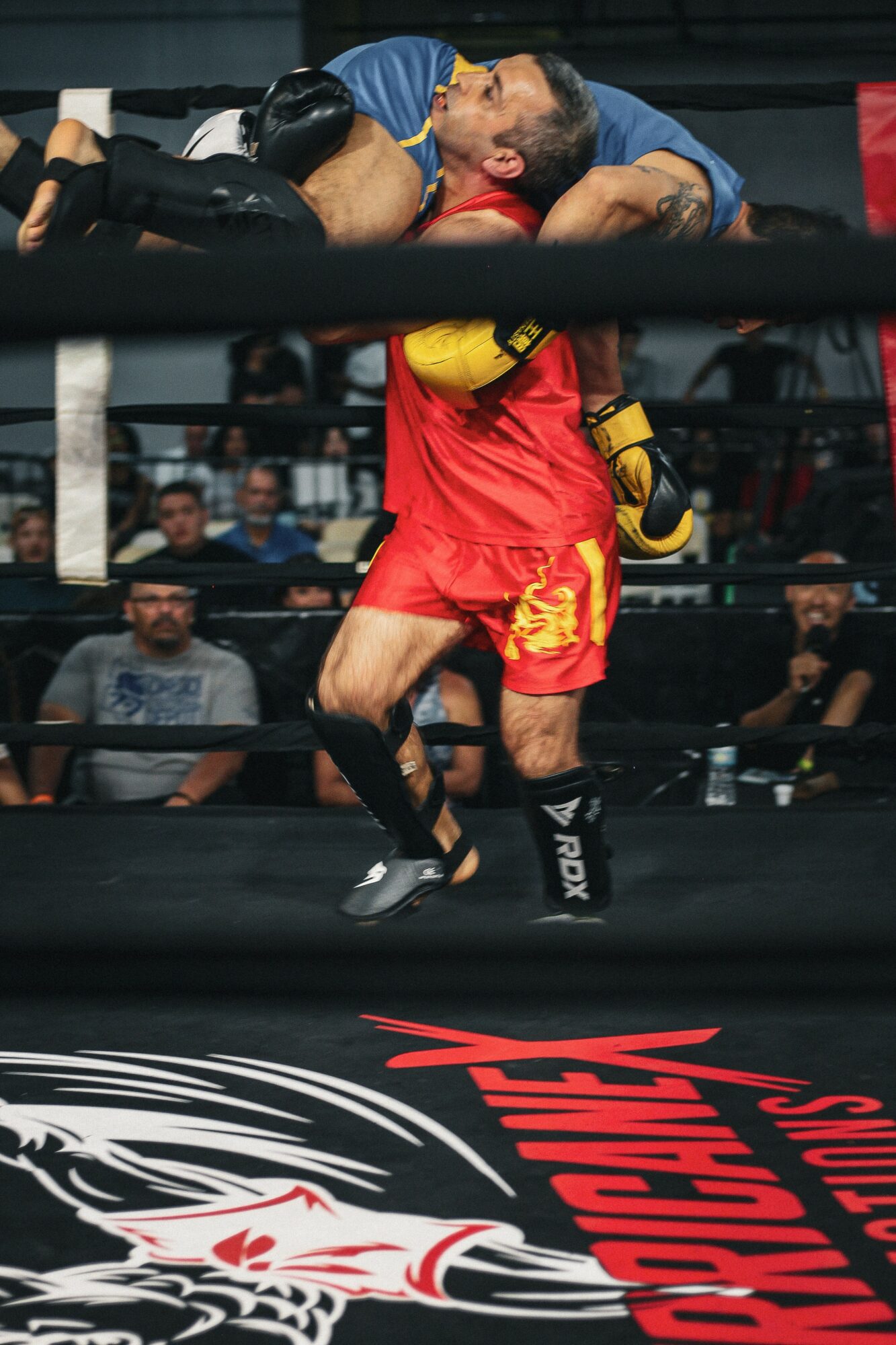 Two fighters in a boxing ring, one in red shorts and the other in blue, engaged in a close combat move.