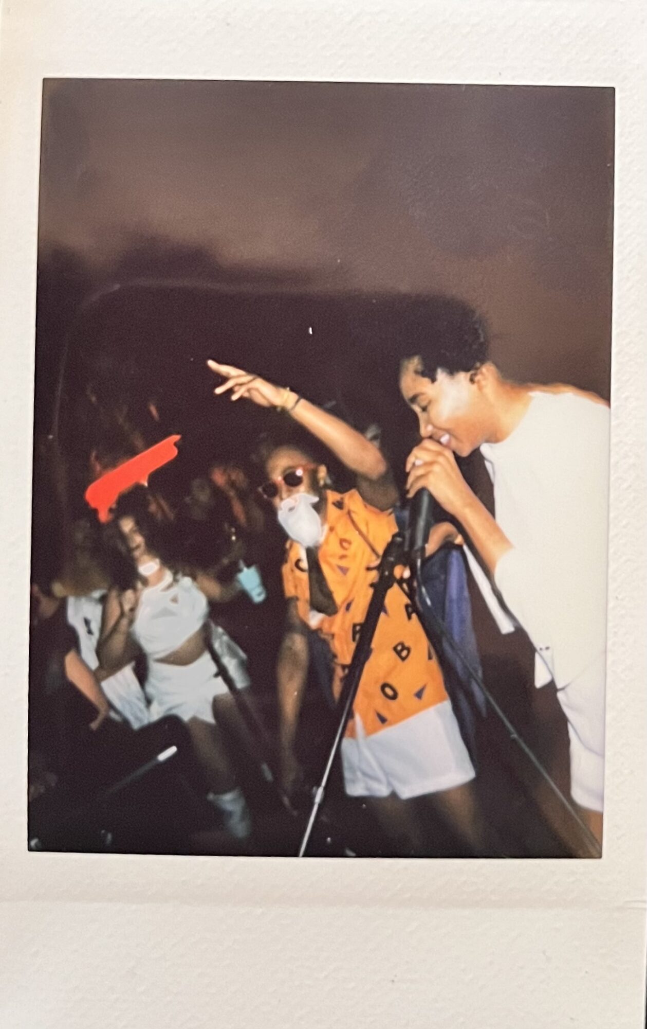 Group of children, one pointing, some wearing masks, in a dark setting with a black background.
