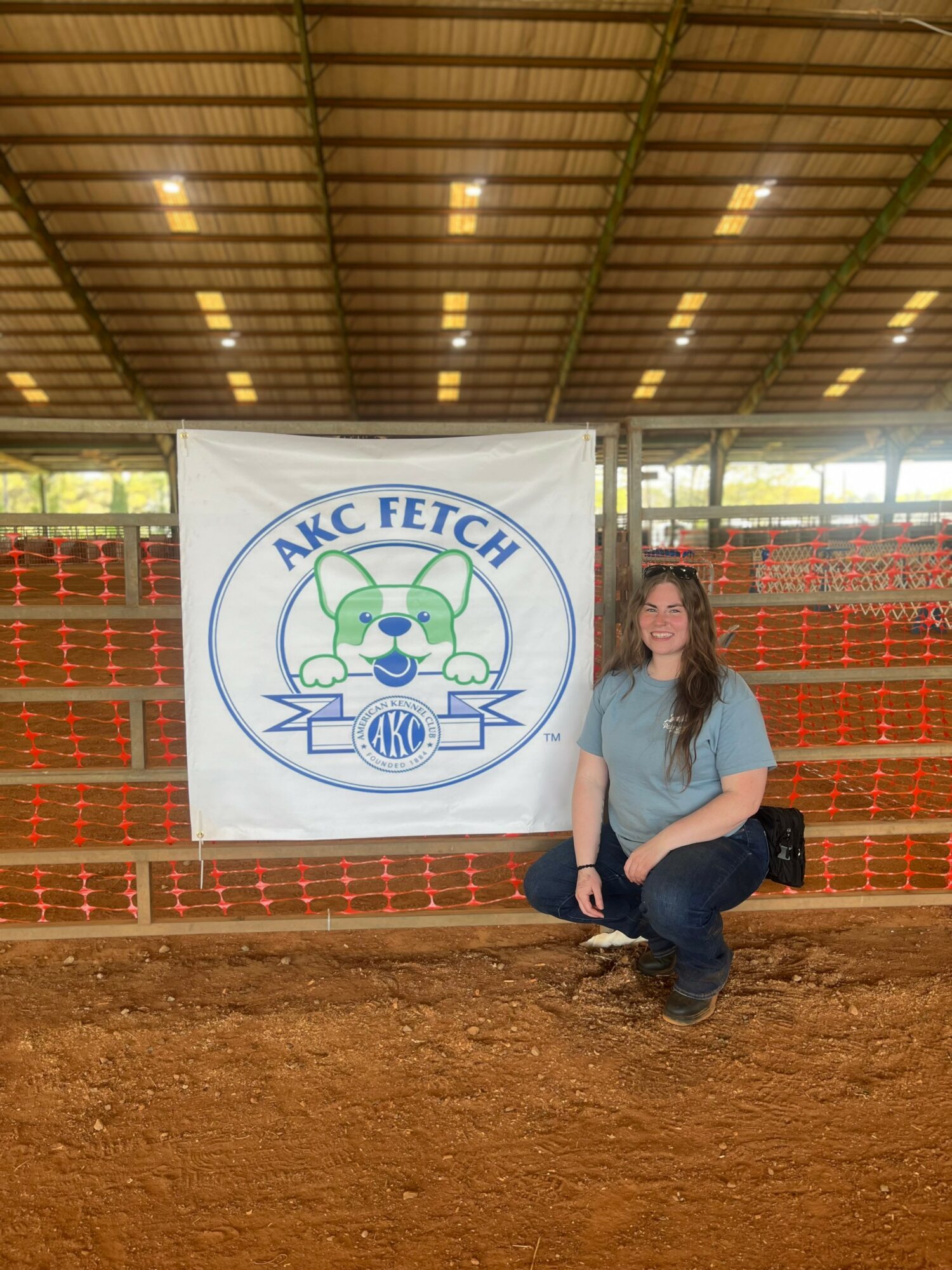 Woman crouching next to a banner with a cartoon car and the text 'ANC FETCH' inside a covered outdoor area.