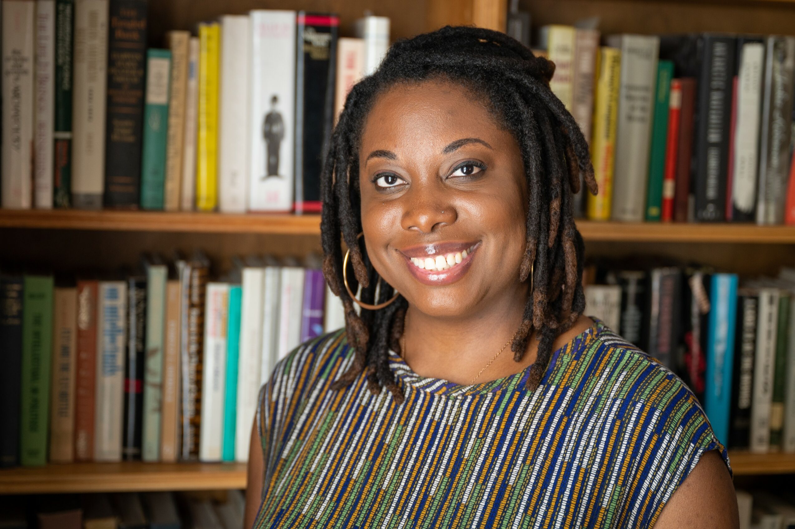 Woman with dreadlocks smiling in front of a bookshelf filled with books