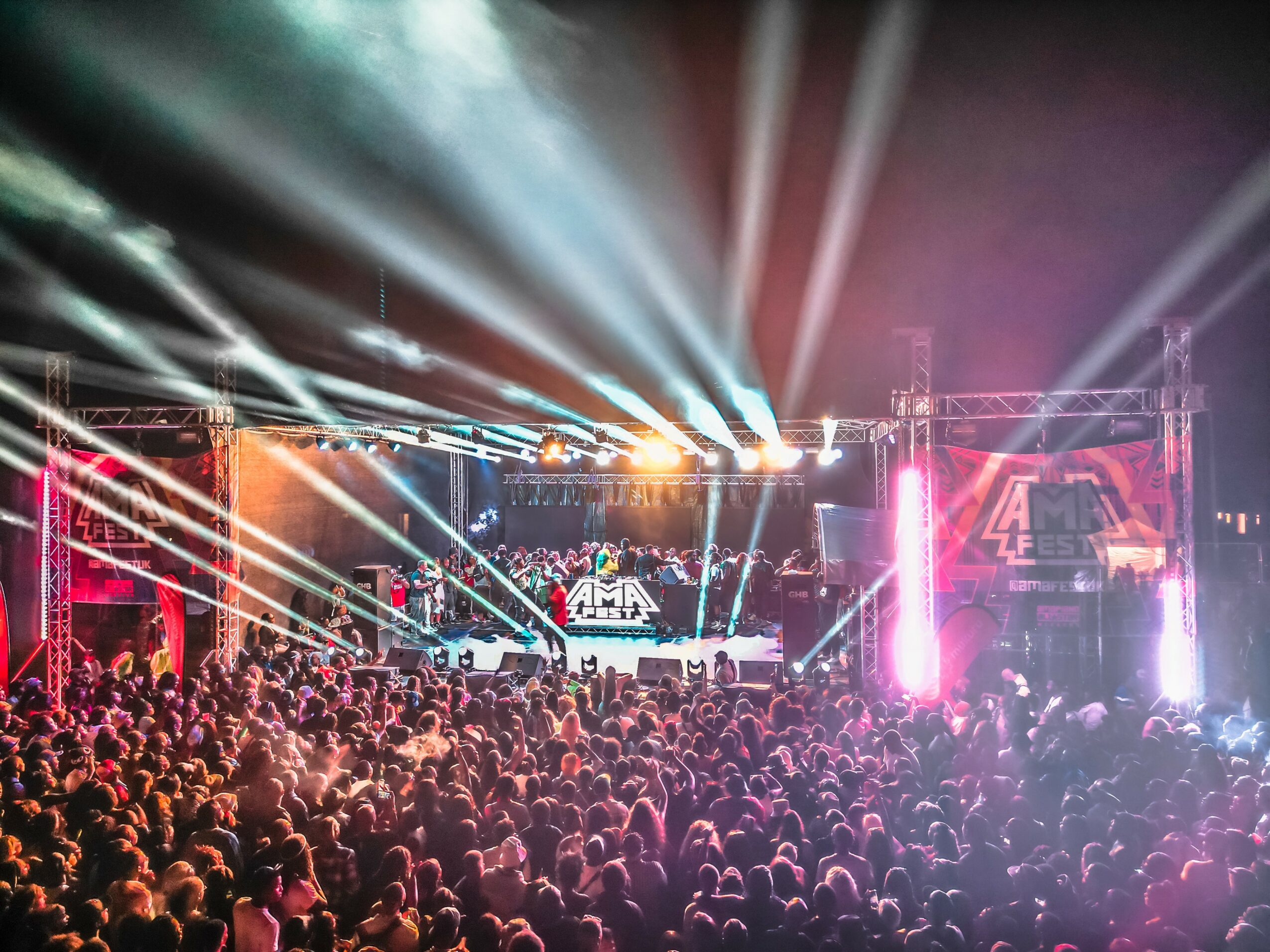 Crowd watching a concert with colorful stage lights and a large screen, stage with performers, vibrant atmosphere.