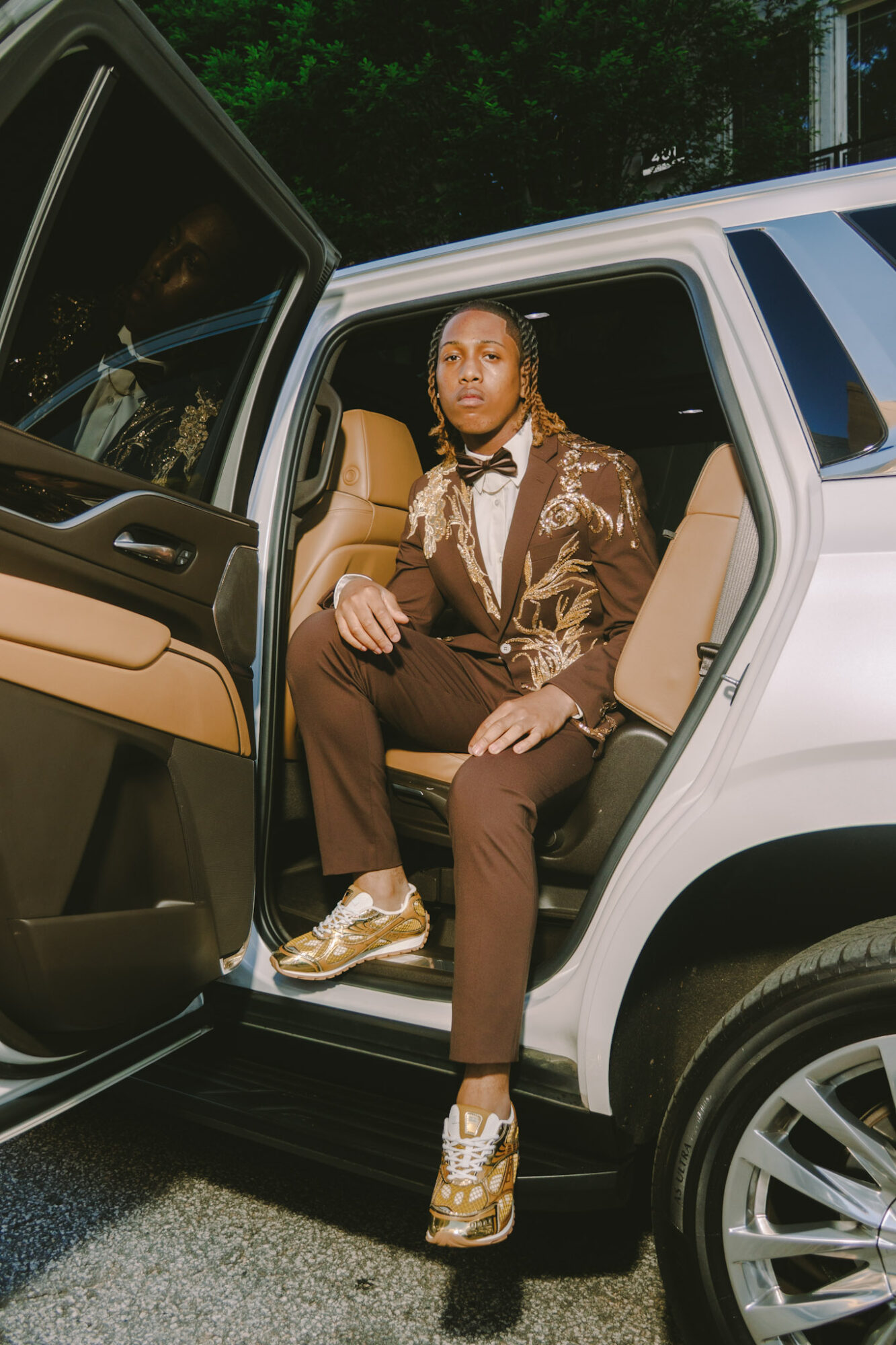 Person sitting in the open car door, wearing a patterned jacket, brown pants, and gold sneakers, outdoors at night.