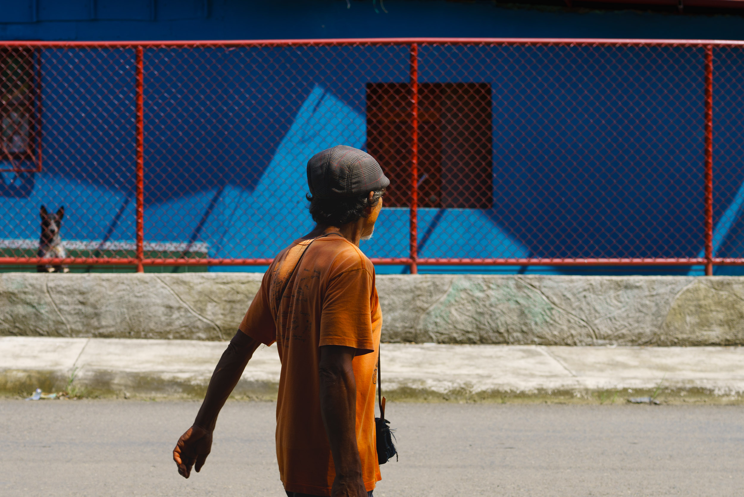 Person wearing an orange shirt and gray cap walking on a street with a colorful mural in the background.