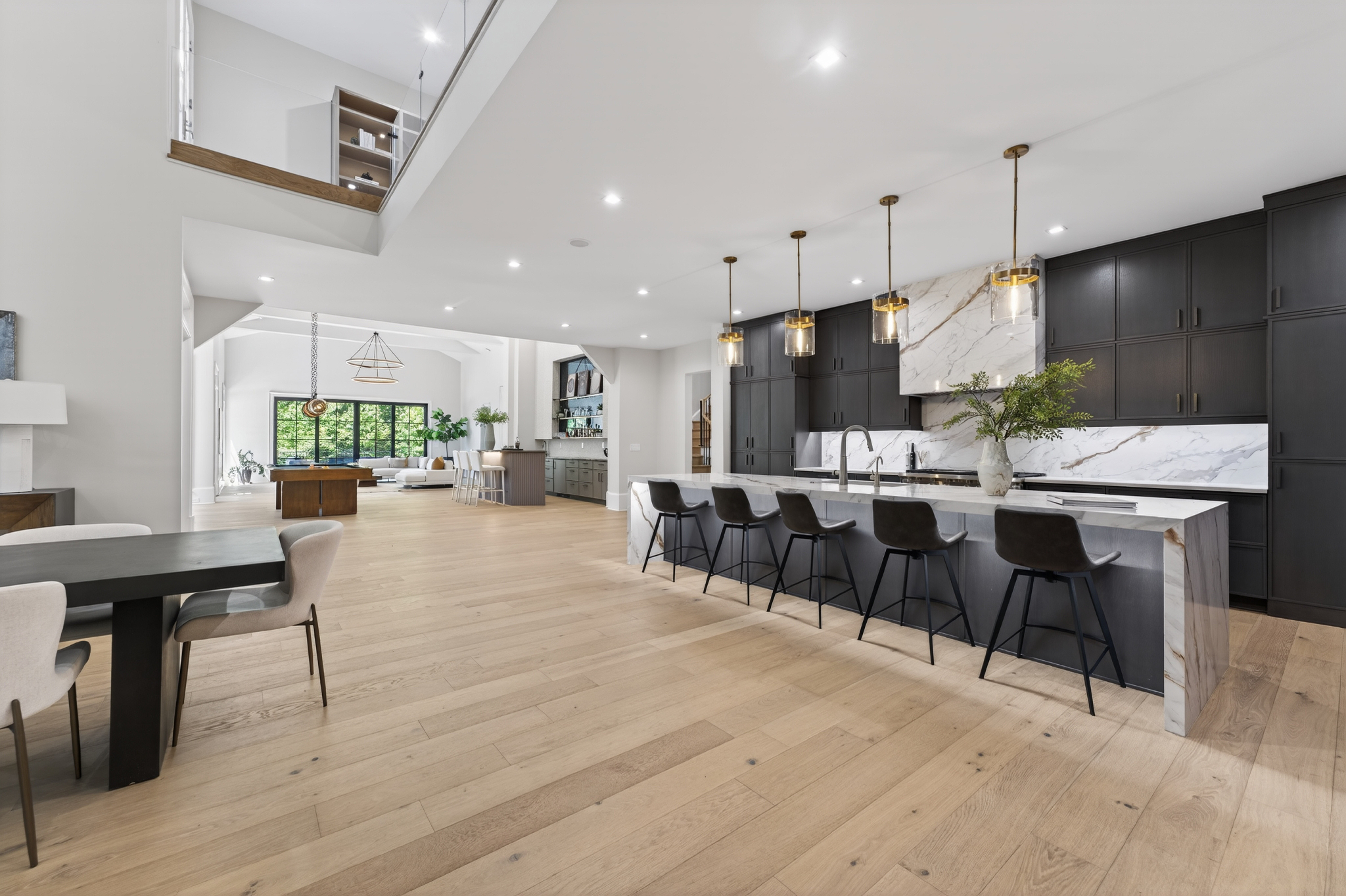 Open-concept kitchen and living area with black cabinets, white countertops, and a large island with barstools, hardwood floors, and modern lighting.