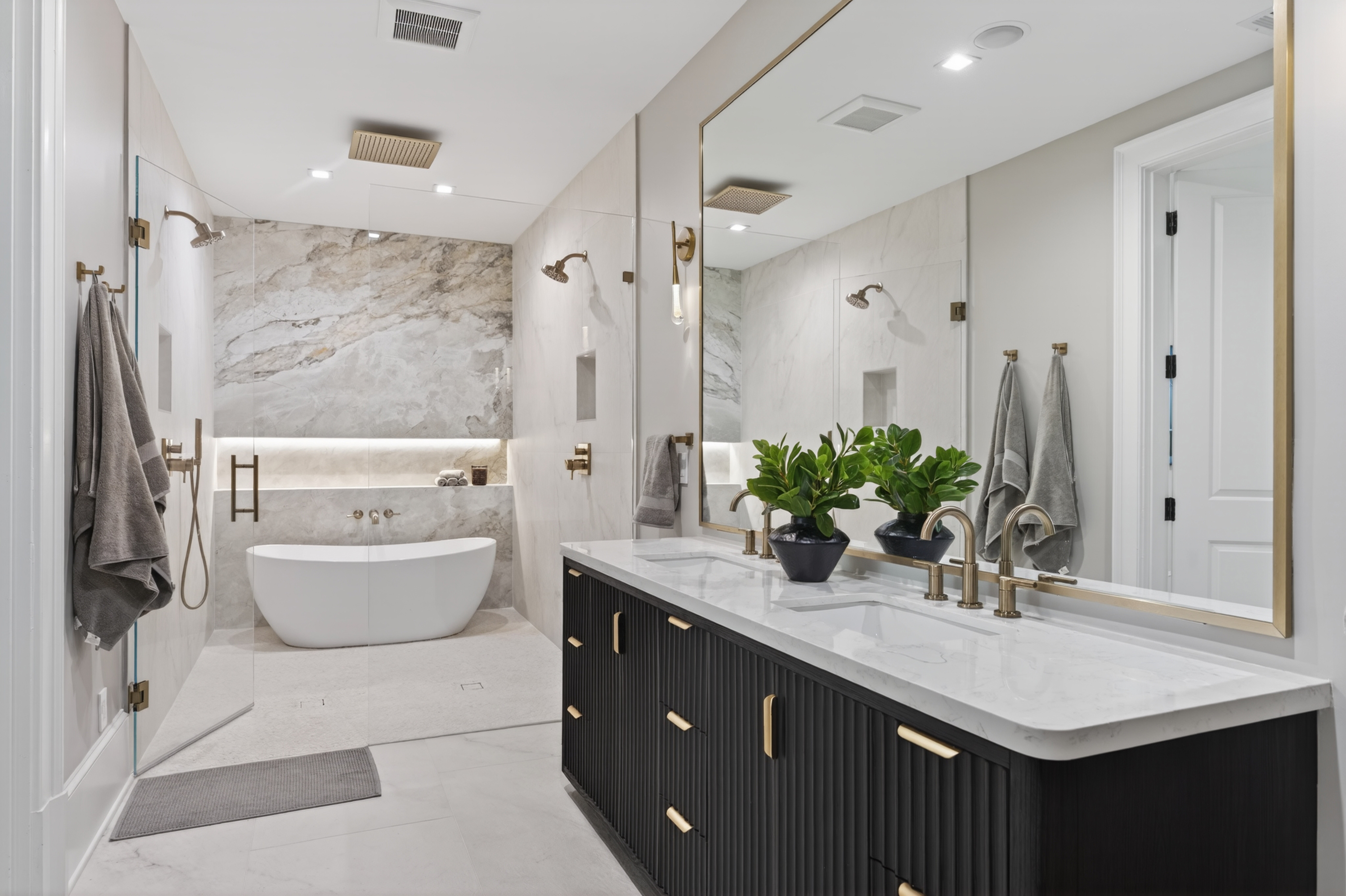 Modern bathroom with a freestanding bathtub, large mirror, and a black vanity with a white countertop, plants, and towels.