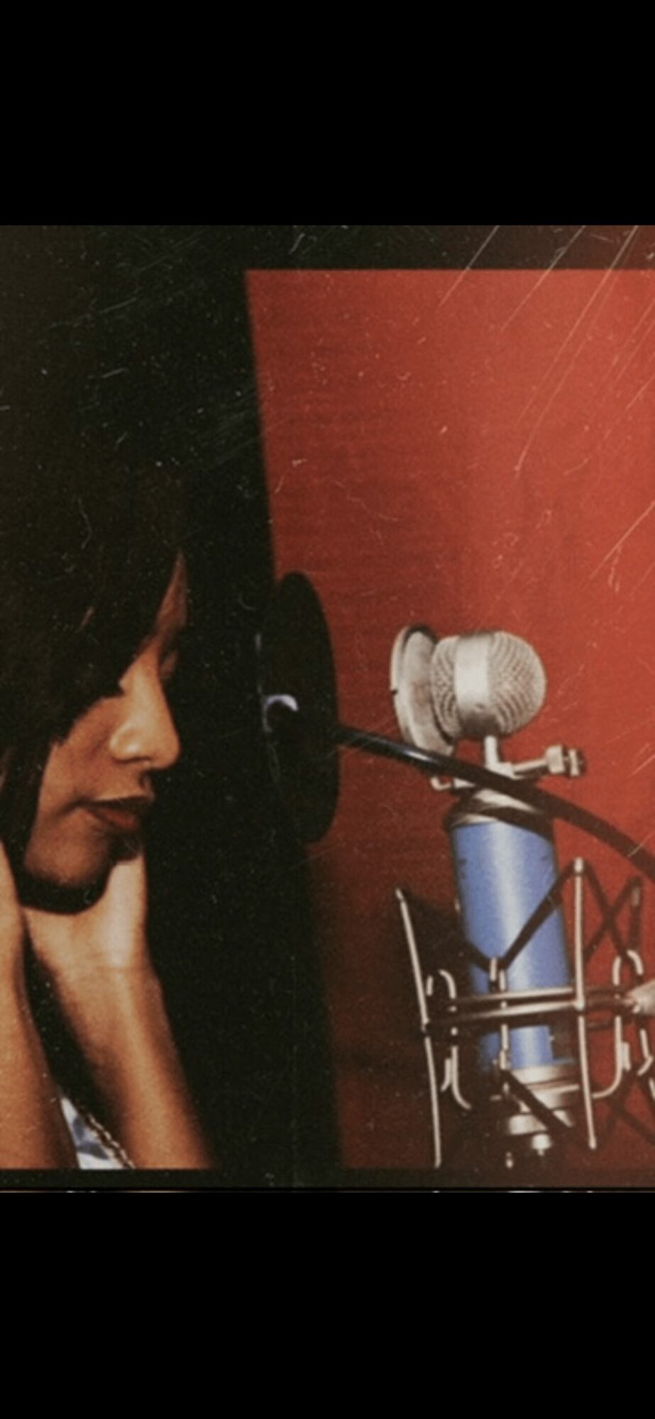 Person with dark hair near a microphone in a recording studio with red and black walls.