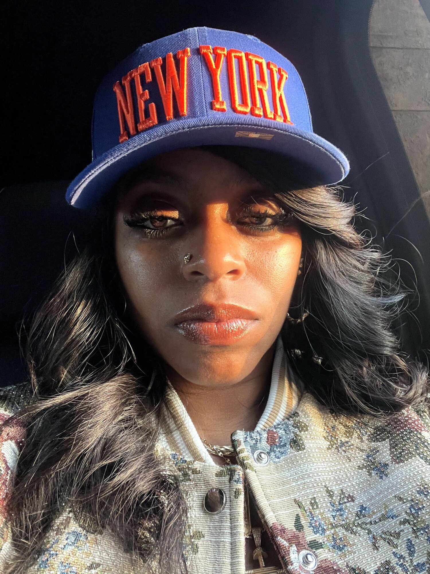 Woman wearing a blue New York cap with long wavy hair, looking directly at the camera.