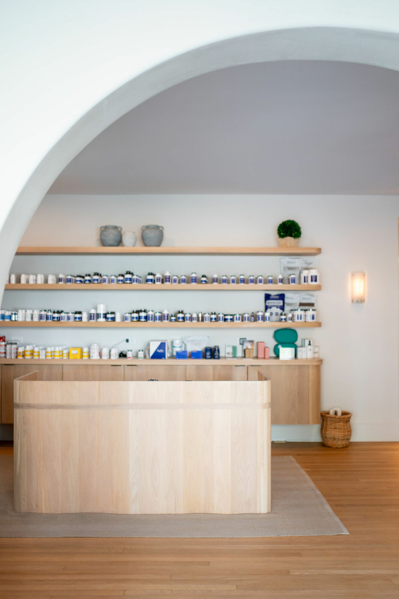 Interior view of a minimalist kitchen with wooden shelves, a countertop, and decorative items, seen through an archway.