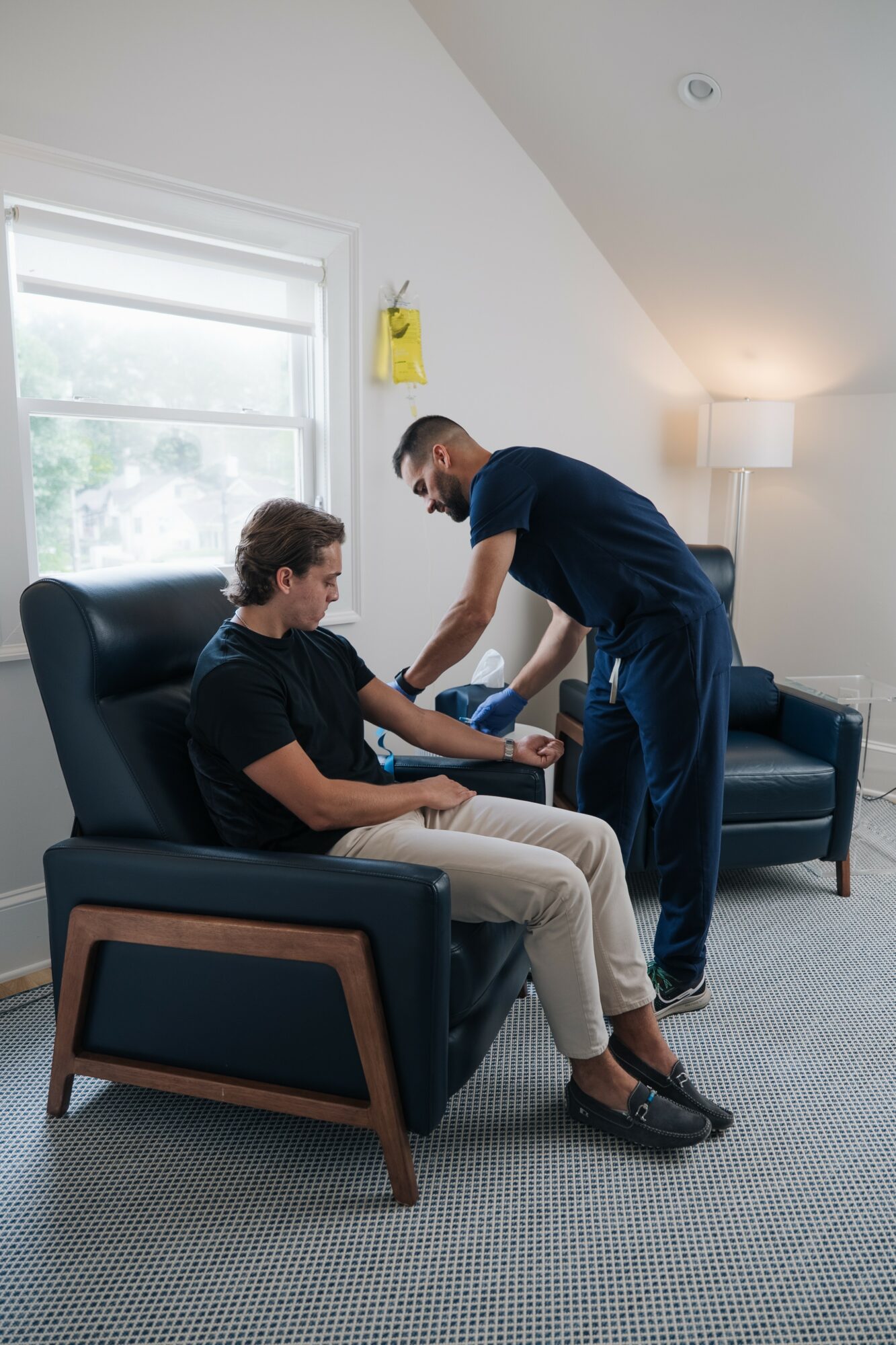 Person sitting in a chair receiving a foot massage from a caregiver in a bright room with a window and lamp
