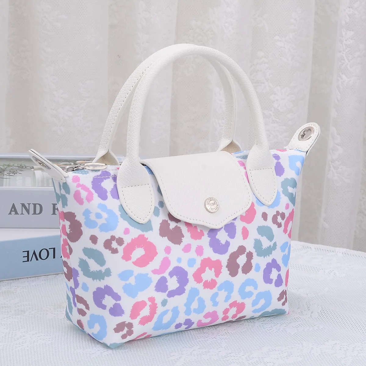 Small handbag with colorful leopard print pattern, white handles, and a flap closure, placed on a white surface.