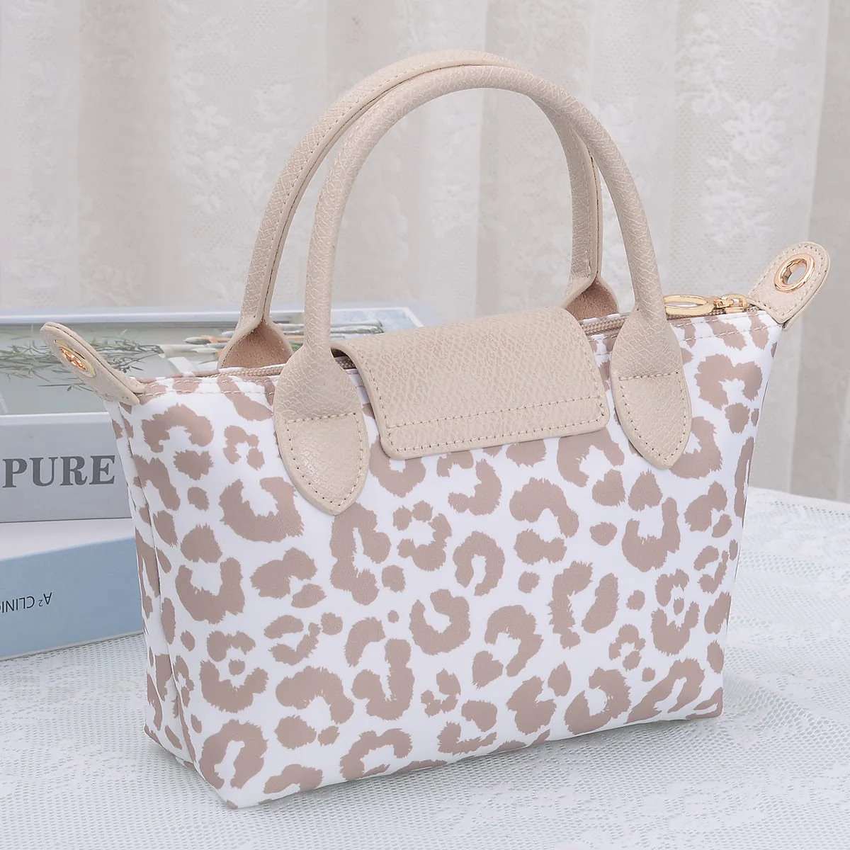 Beige and white leopard print handbag with handles and a flap, placed on a white surface.