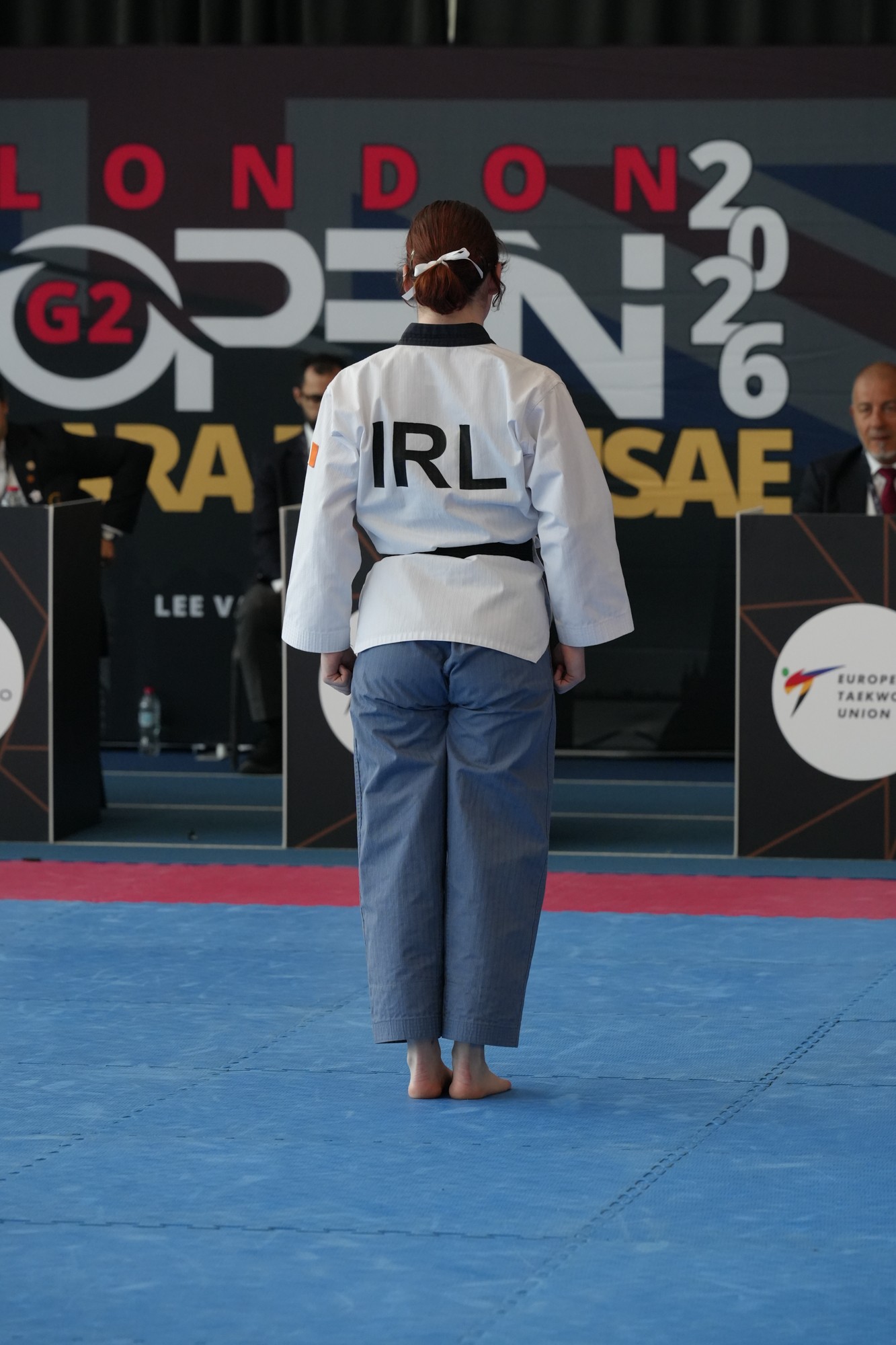 Person in a martial arts uniform with 'IRL' on the back, standing on a blue mat at a competition.