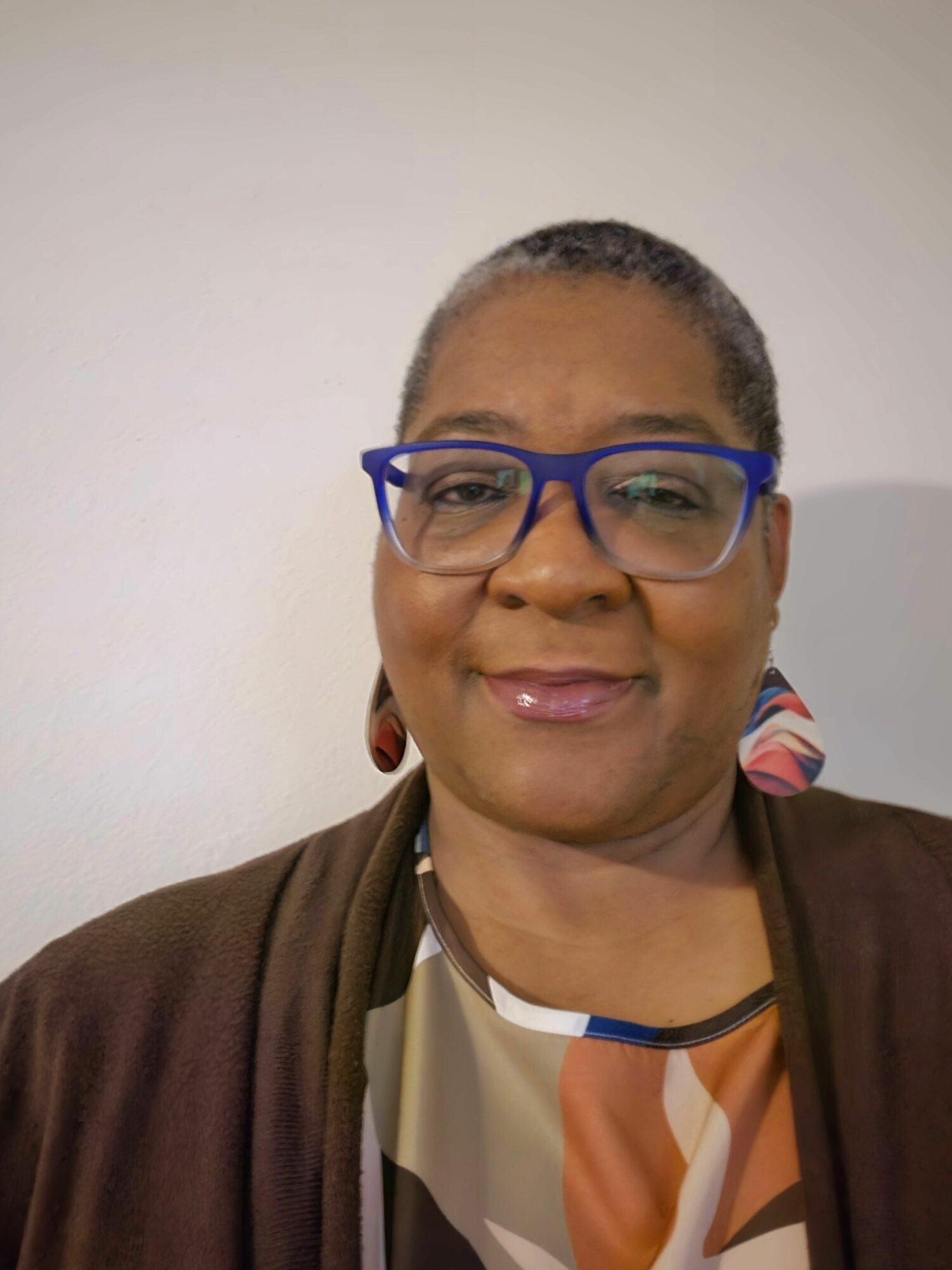Portrait of a woman with glasses, smiling, against a plain background.