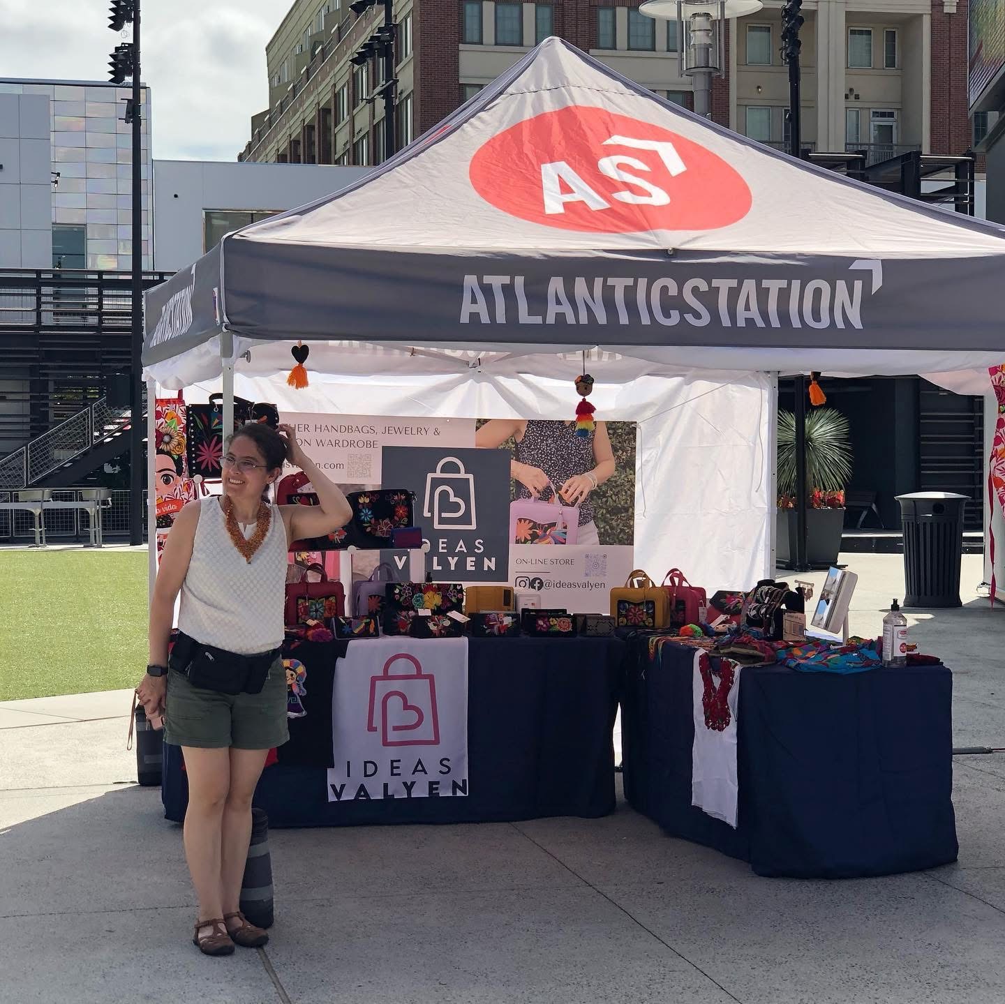 Woman standing in front of a booth with a tent labeled 'ATLANTICSTATION' and 'IDEAS VALLEY' at an outdoor event.
