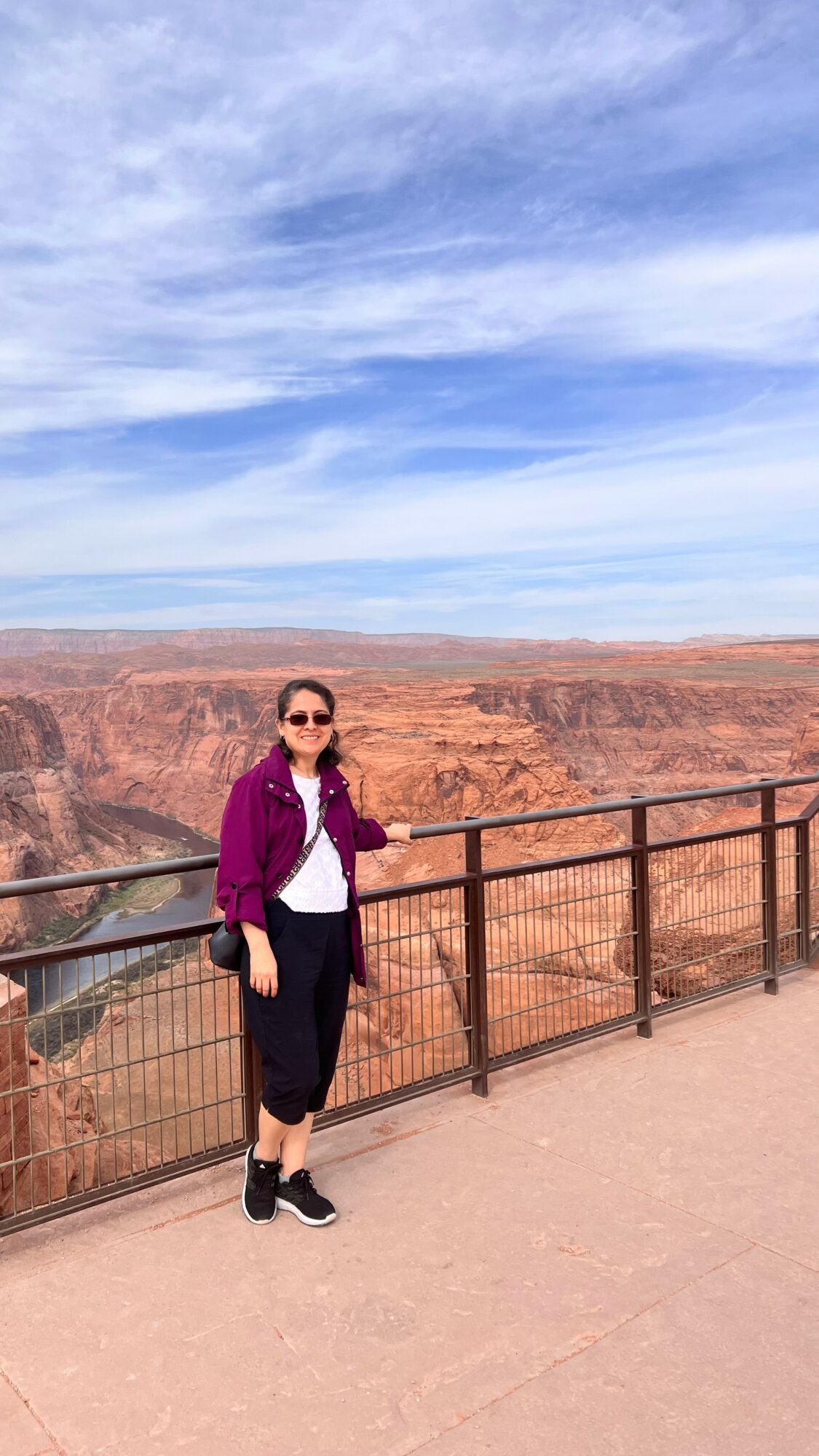 Person standing by a railing overlooking a canyon with blue sky and clouds above.