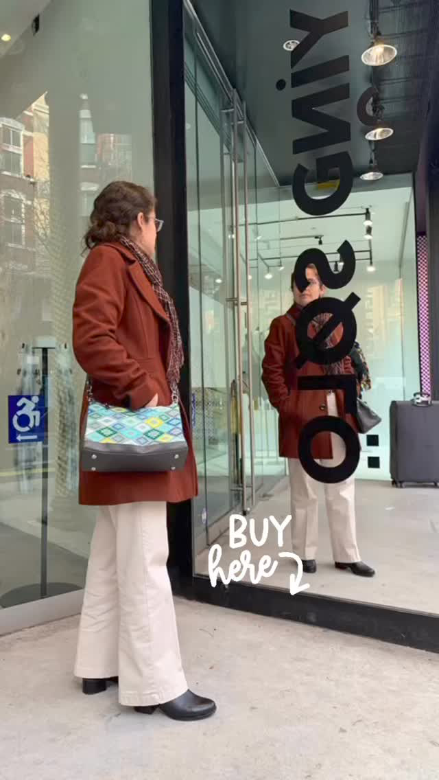 Two women stand outside a glass storefront, one looking at her reflection, with a sign that says 'BUY here'.