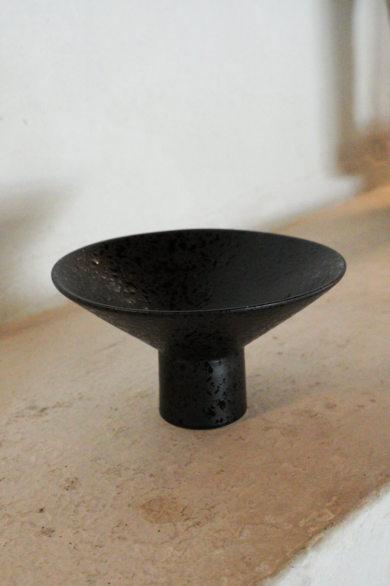 Black ceramic bowl with a wide, shallow shape on a beige surface, against a light background.